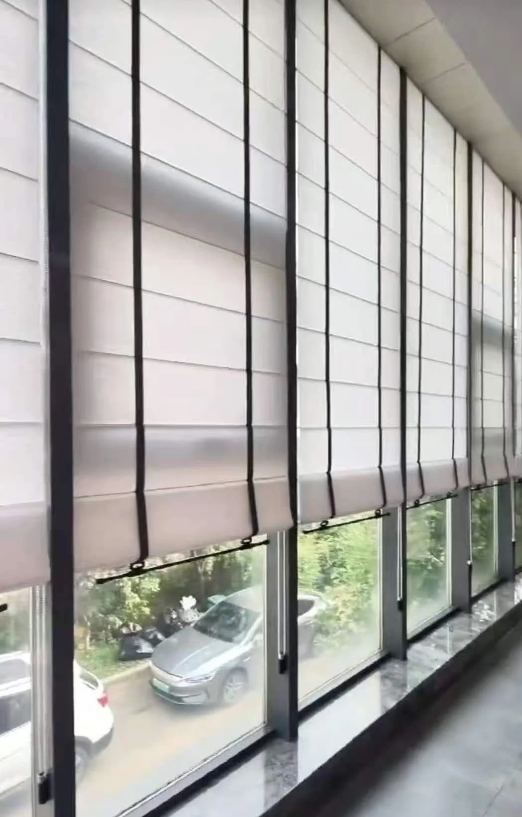 A series of stylish white Roman blinds partially cover large windows overlooking a garden