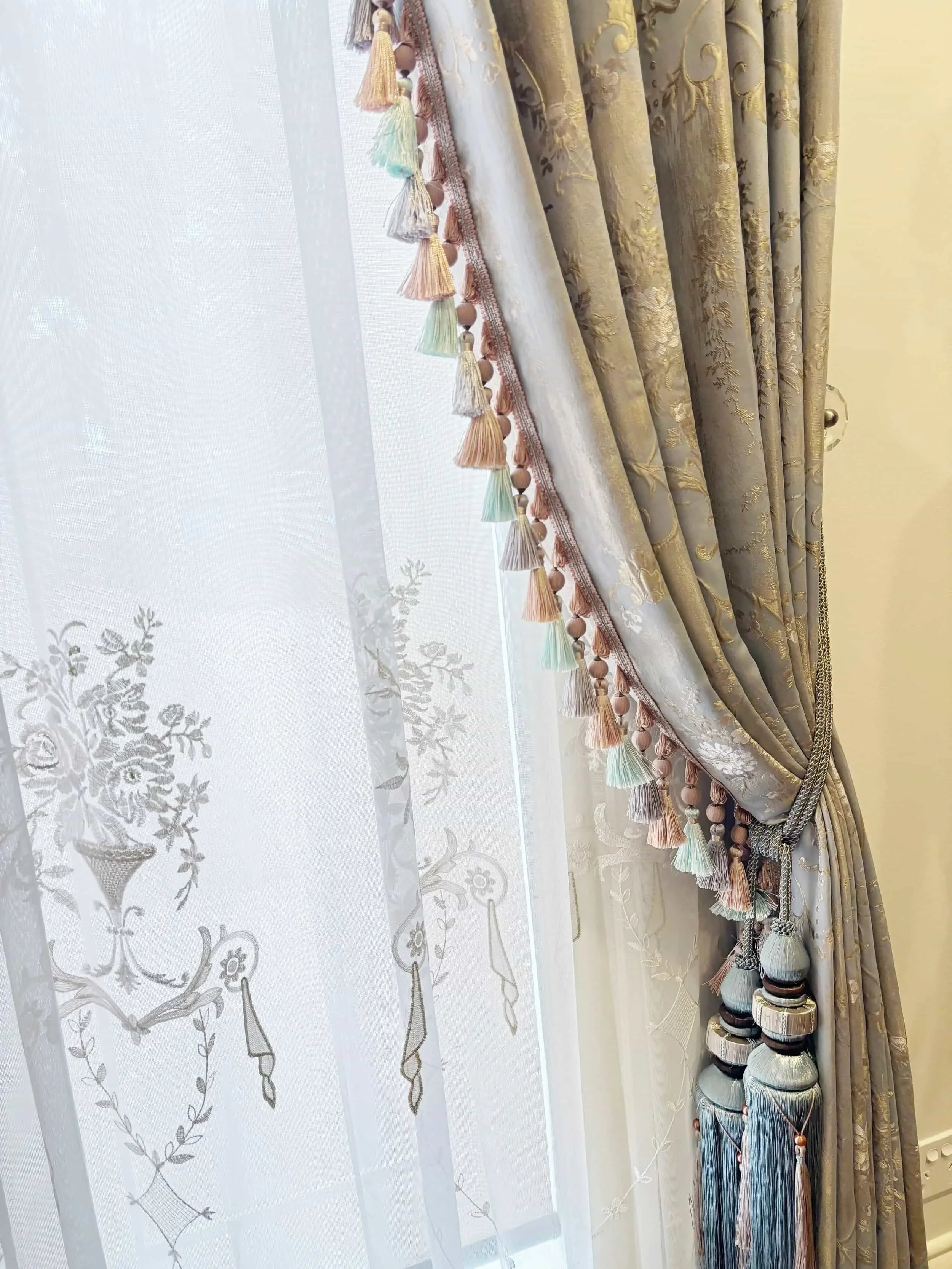 Elegant curtains with tasseled trim and floral sheer drapes, tied back with decorative tassels