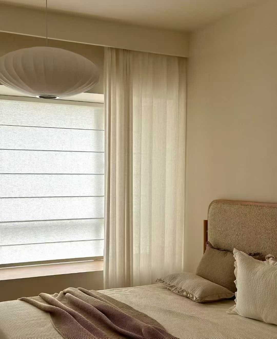 Minimalist bedroom with soft beige tones complimented by Roman blinds and sheer curtains