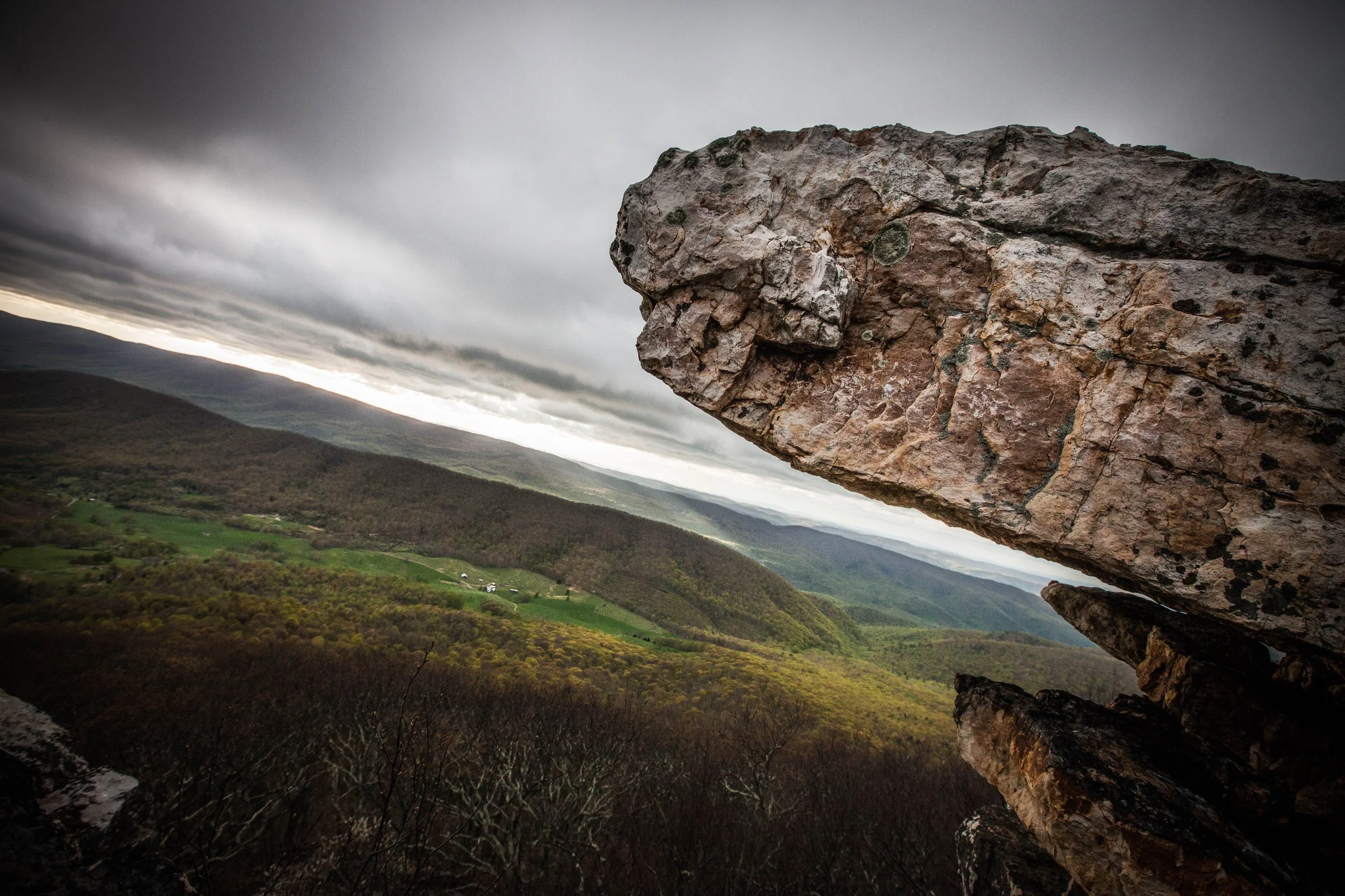 View of a lush green valley with rolling hills under a cloudy sky, seen through large rock formations in the foreground.