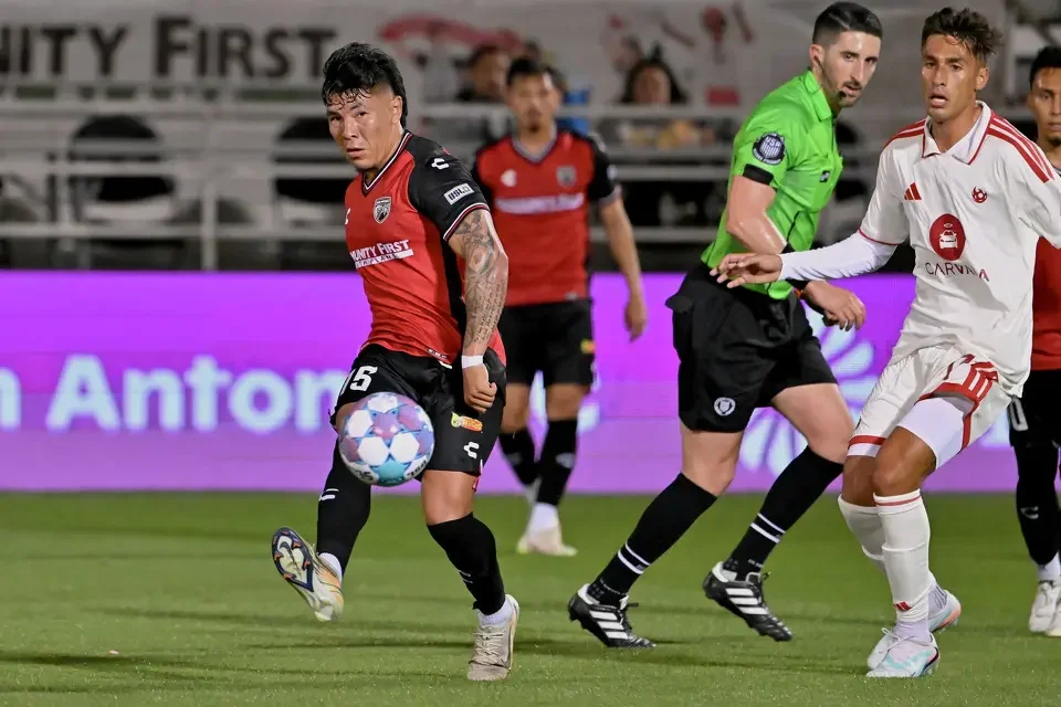 Soccer player in red jersey controlling the ball, surrounded by players and a referee on the field.