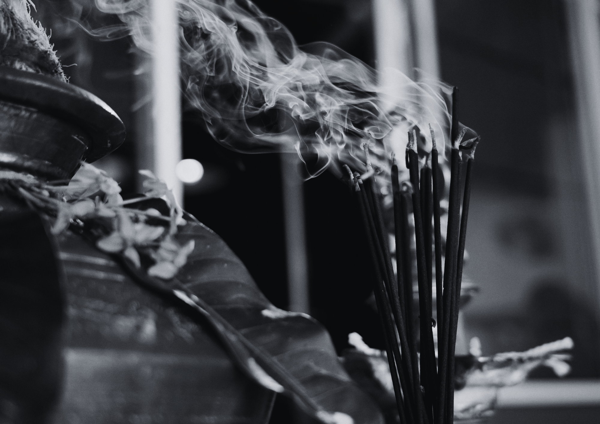 Close-up of smoking incense sticks on a table with decorative leaves in black and white.