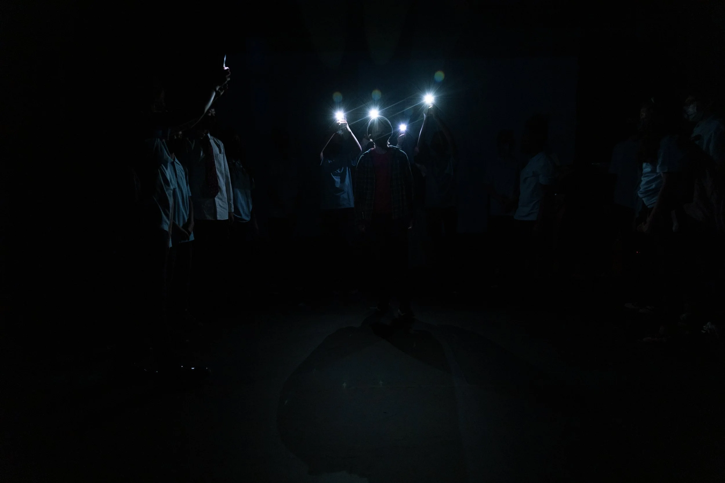 People in a dark room holding flashlights above their heads, creating a star effect.