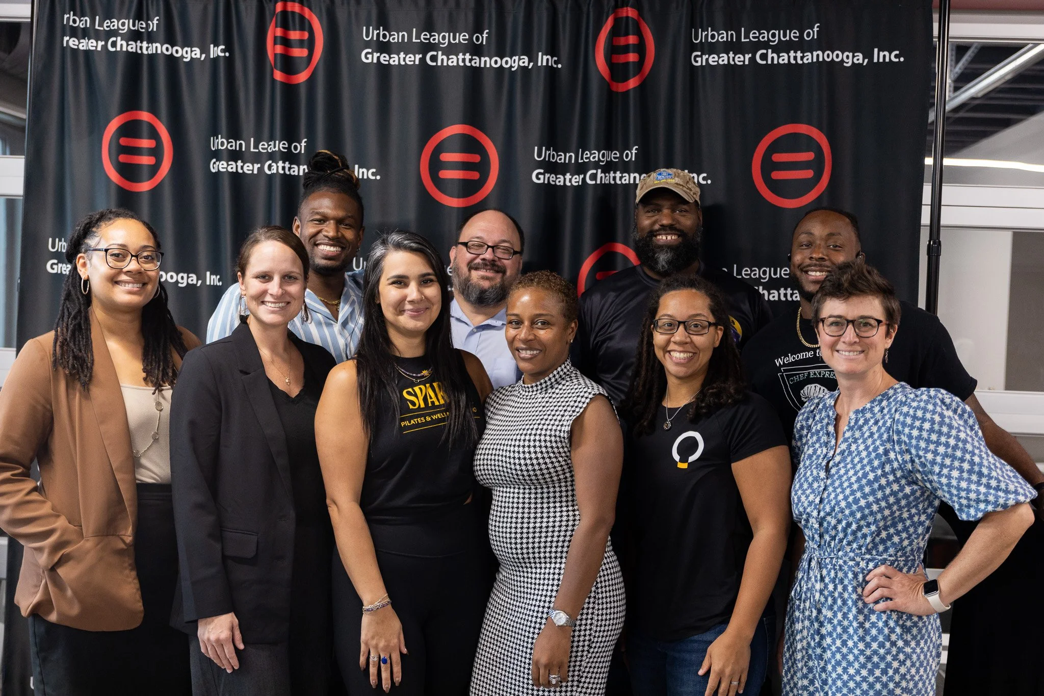 A diverse group of ten women and men standing together at an event for the Urban League of Greater Chattanooga, Inc., in front of a black backdrop with red and white logos and text.
