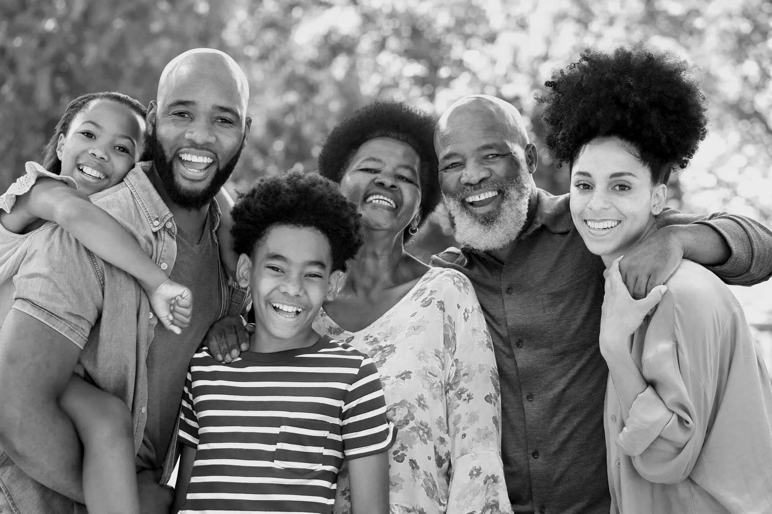 Family of six outdoors, smiling, hugging, in black and white.
