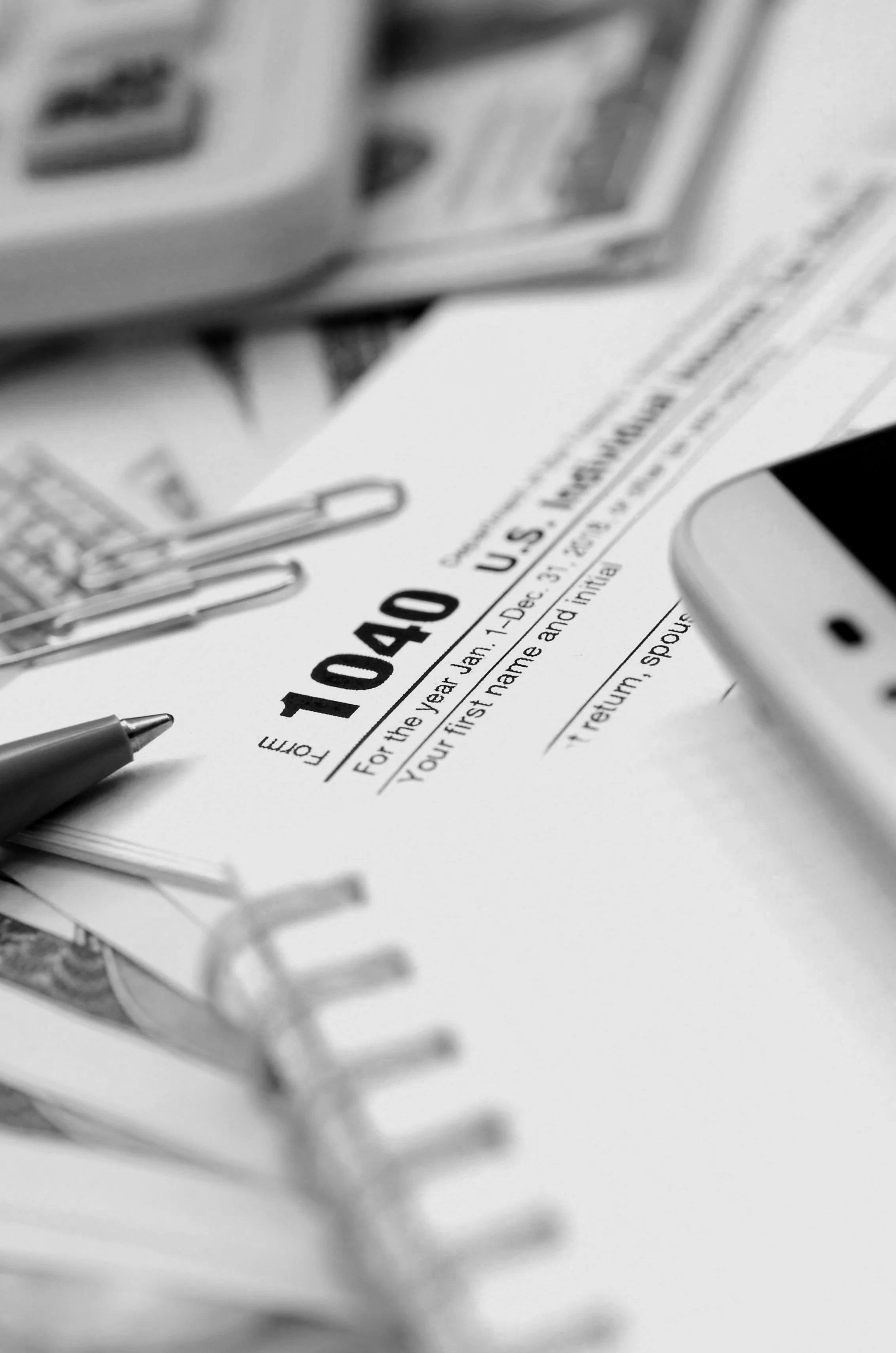 A pen and paper work visa application form, with documents and office supplies around, in black and white.