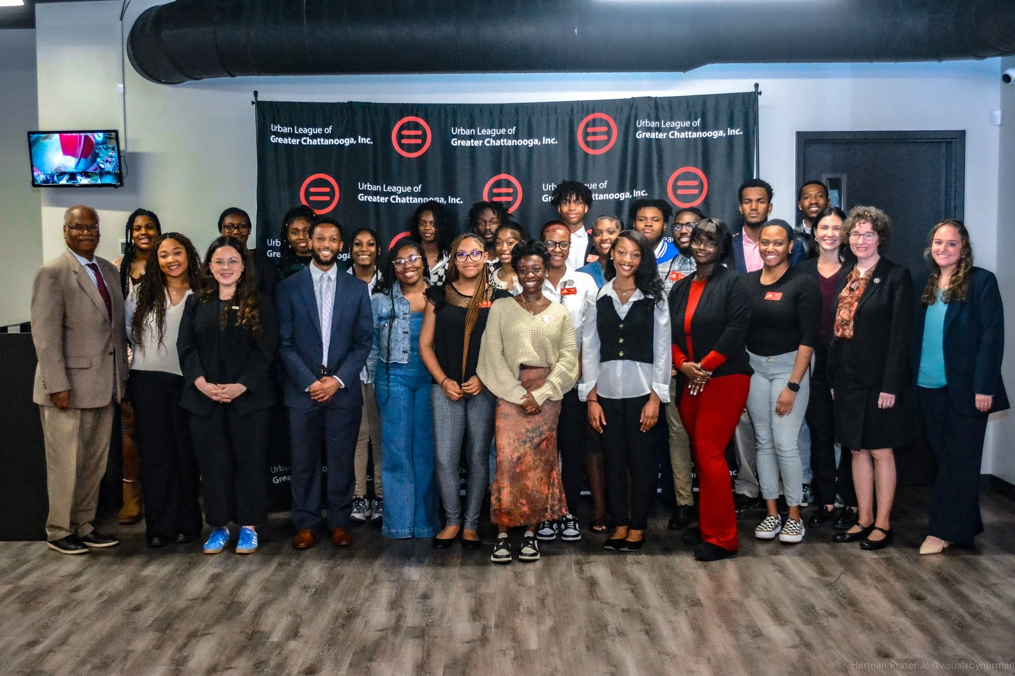 Group photo of diverse people standing in front of a black backdrop with the logo of Urban League of Greater Chattanooga, Inc. indoors, some smiling and dressed in professional attire.