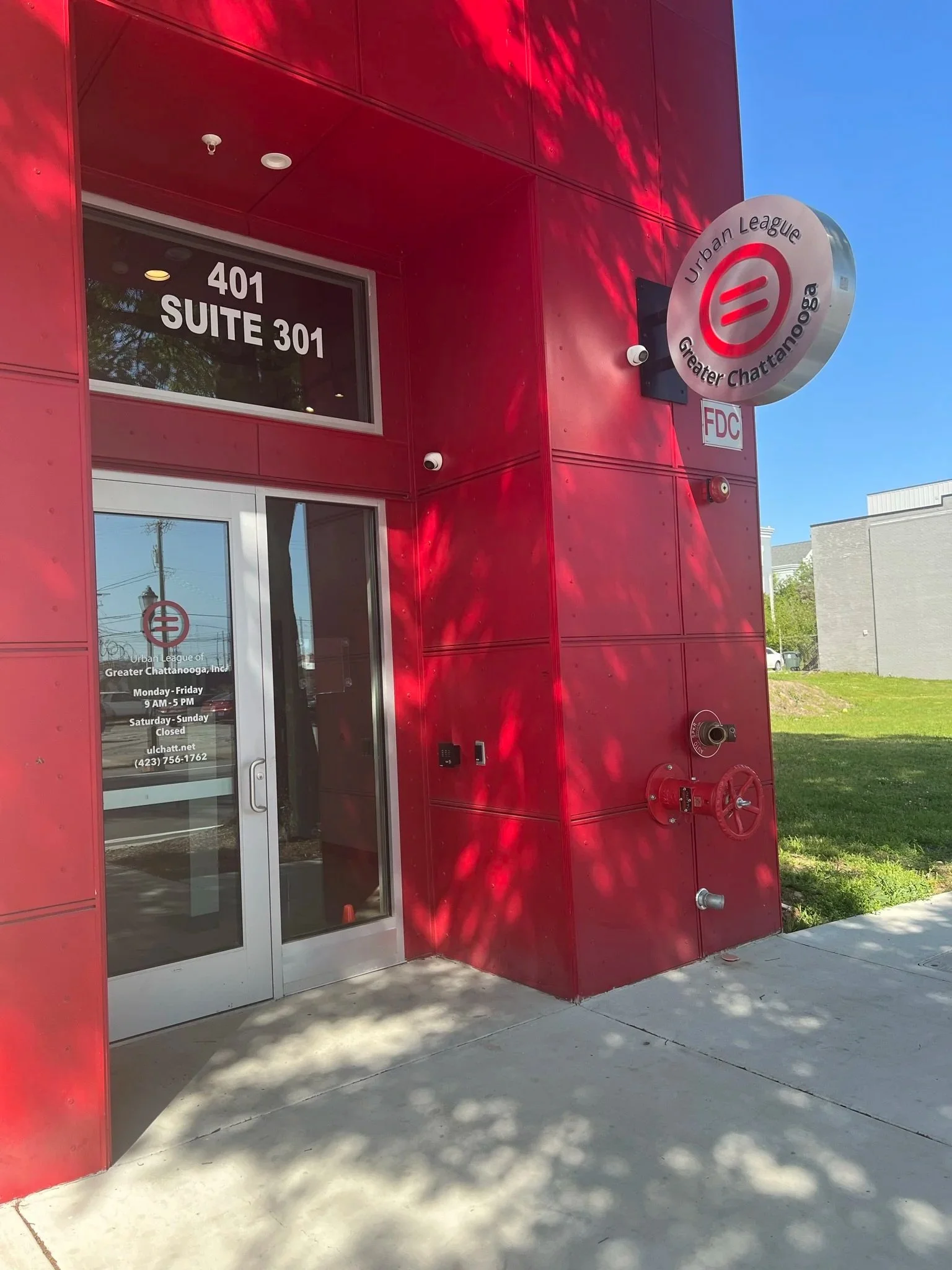 Red exterior of a building with a sign for the Urban League Greater Chattanooga, including address numbers 401 and suite 301, and a glass door with hours of operation and contact information.