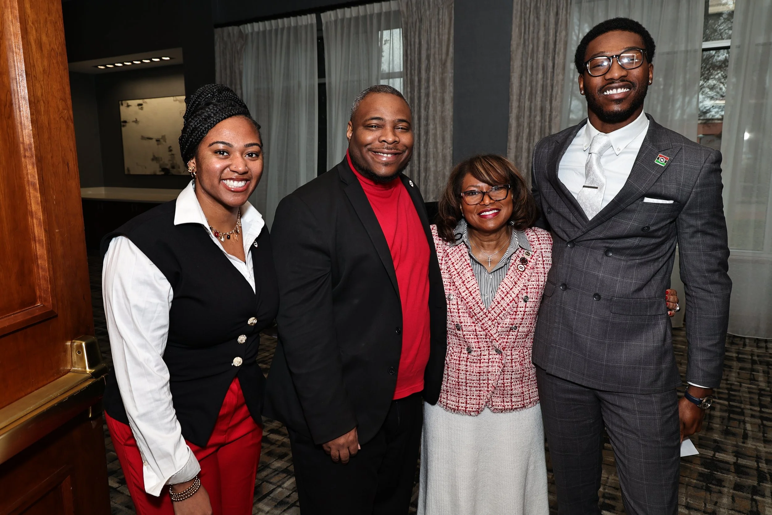 Group of five diverse people standing together indoors, smiling for the photo.