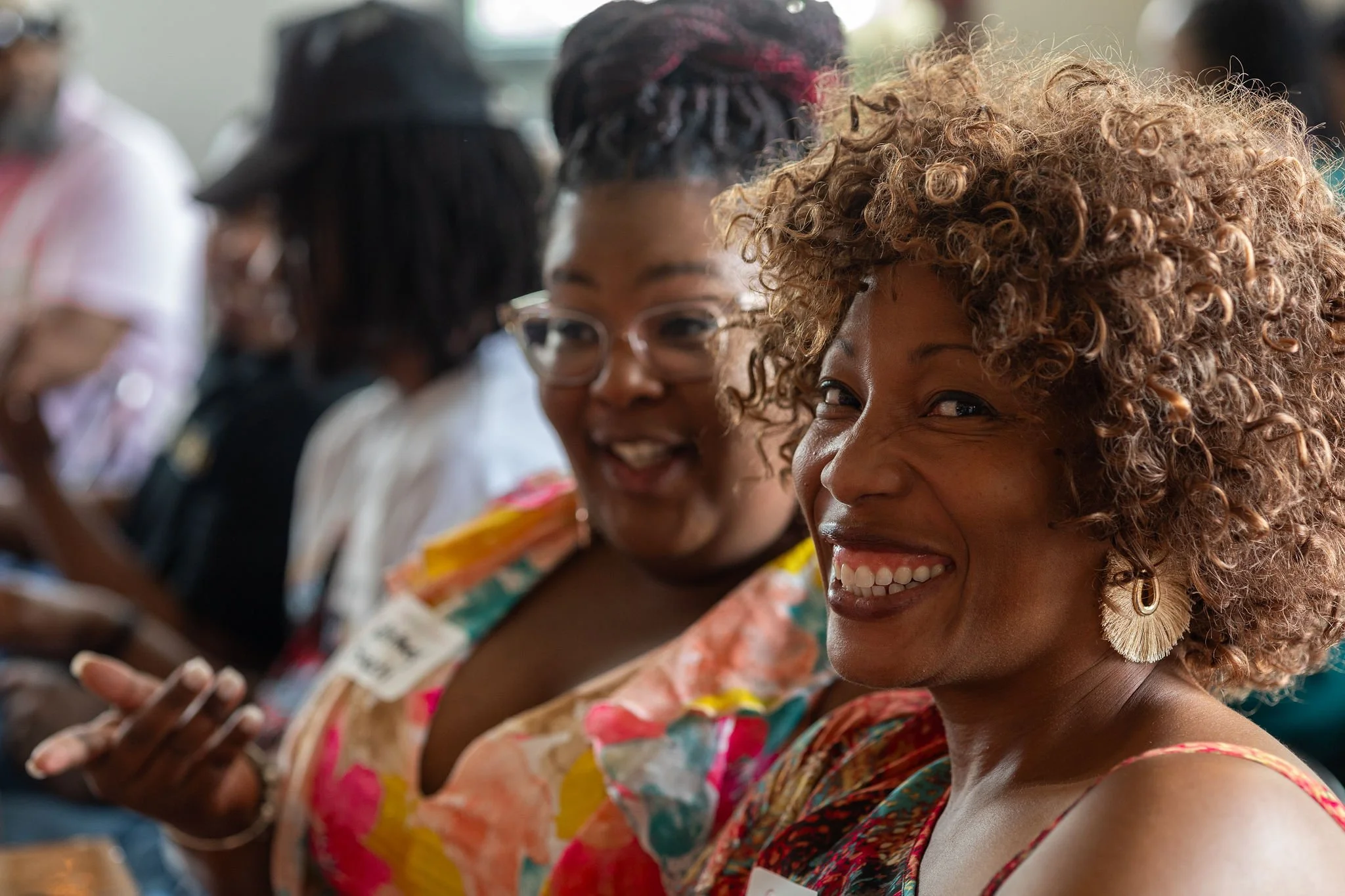 Two women sitting together, smiling and engaging in conversation at a social event.