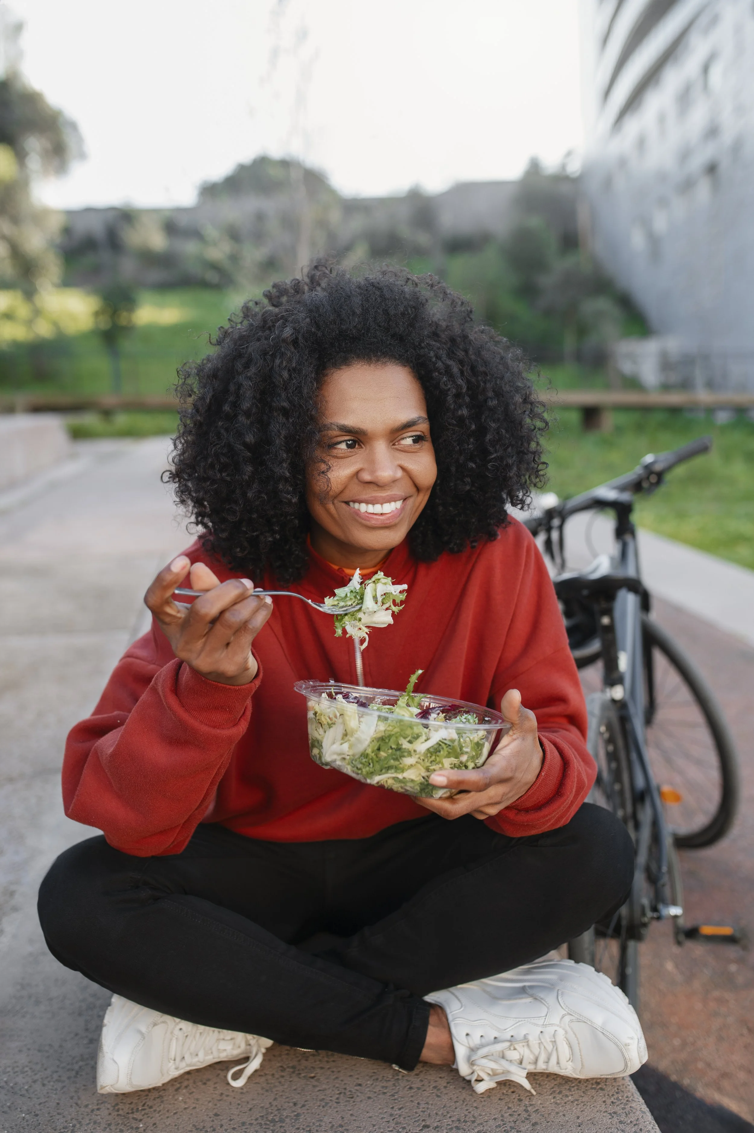 Woman sitting cross legged outside while eating a salad