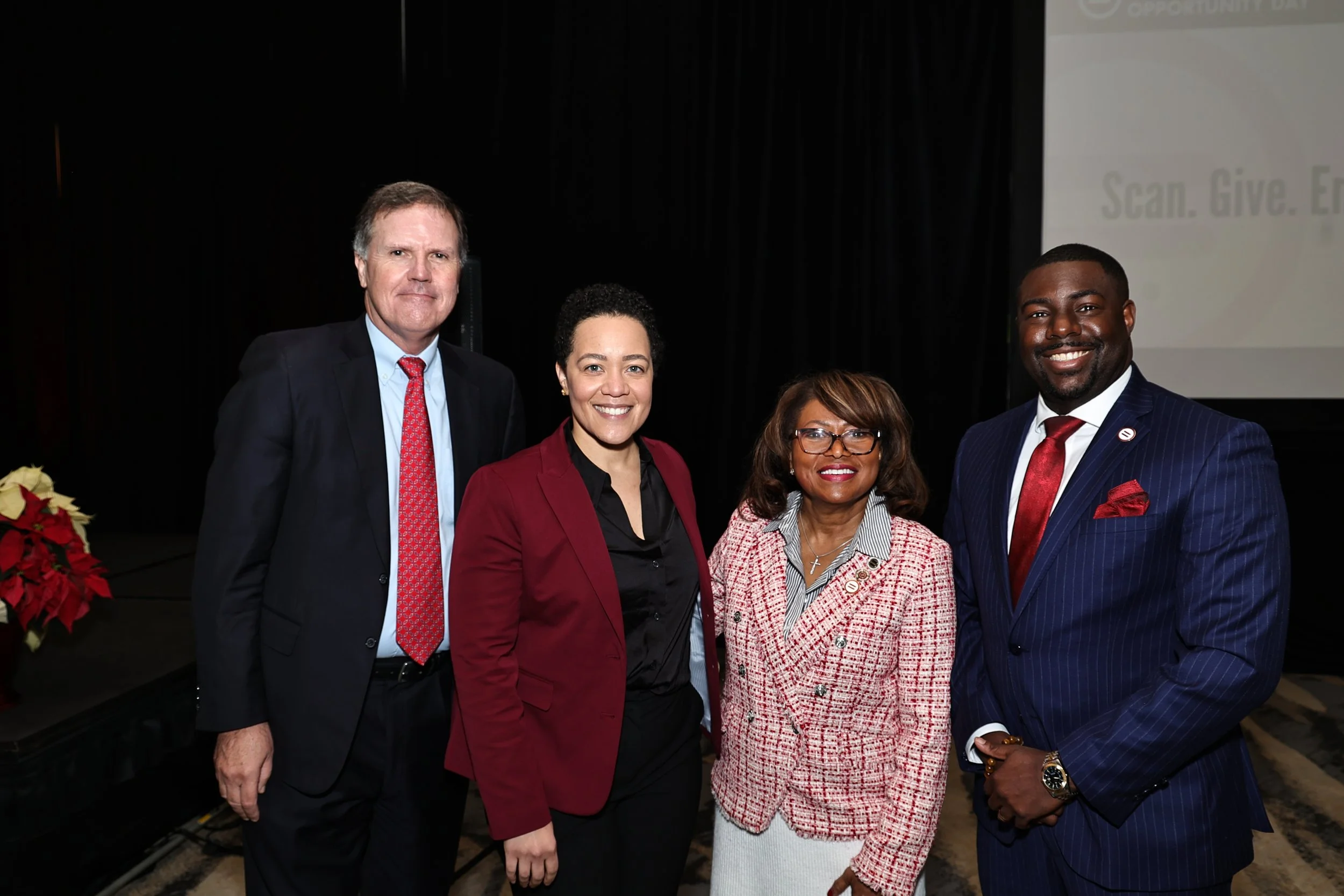 Five professionally dressed people standing together indoors, smiling for a photo during a formal event.