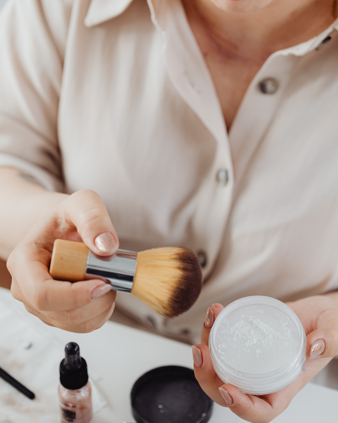 Person holding powder and makeup brush in hand, applying makeup or skincare product.