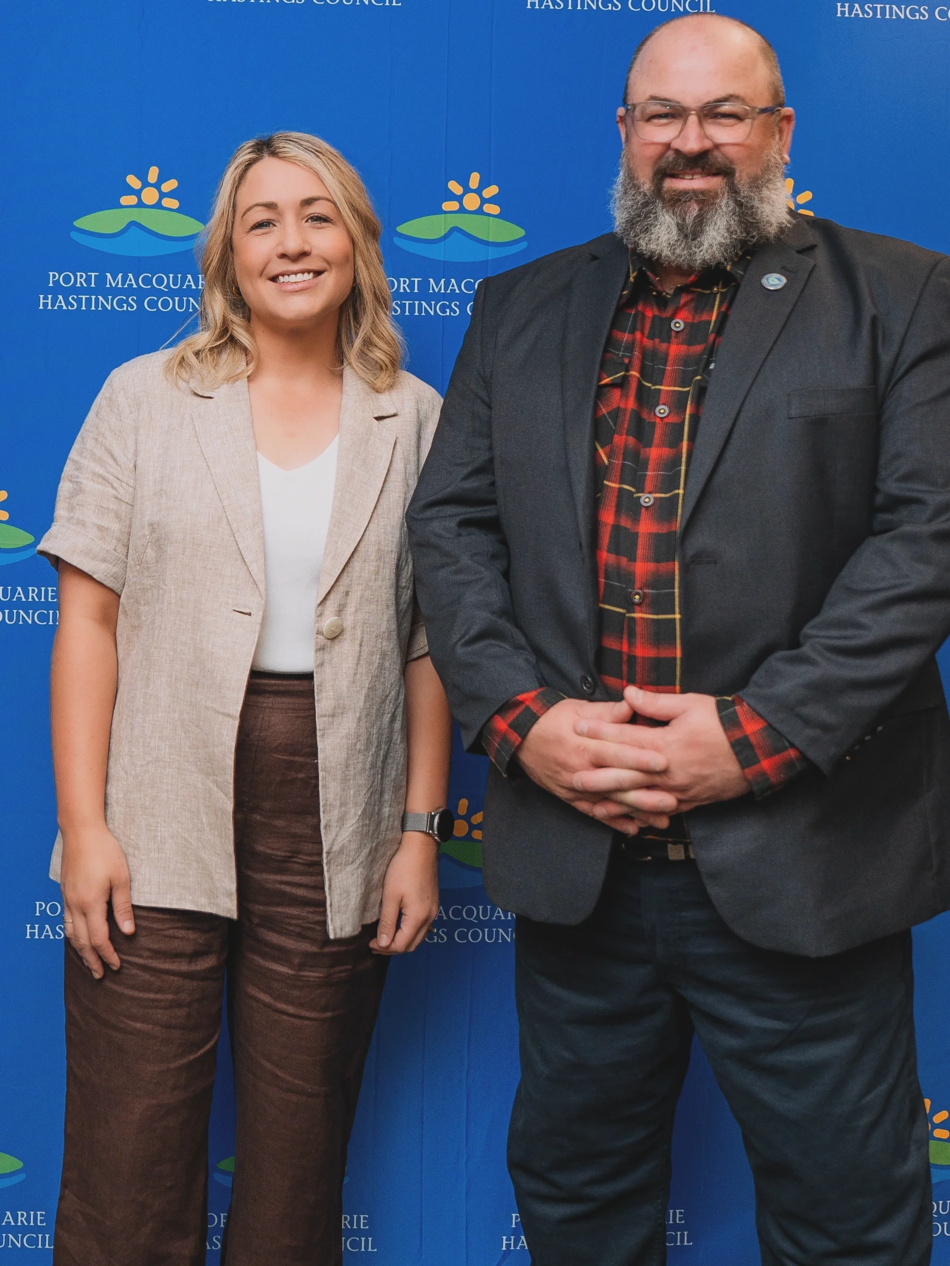 Two people standing in front of a blue backdrop with the text 'Port Macquarie Hastings Council'. The woman on the left is the My Selfcare Founder. The man on the right is the current Mayor of Port Macquarie Hastings Council.