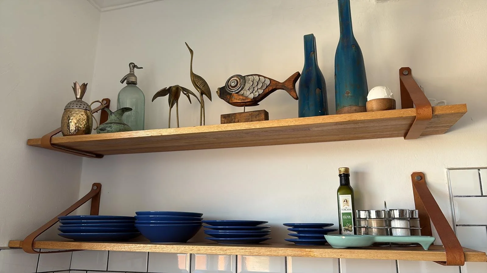 Wooden kitchen open shelves with decorative bottles, sculptures, blue plates, a bottle of olive oil, and spice jars.