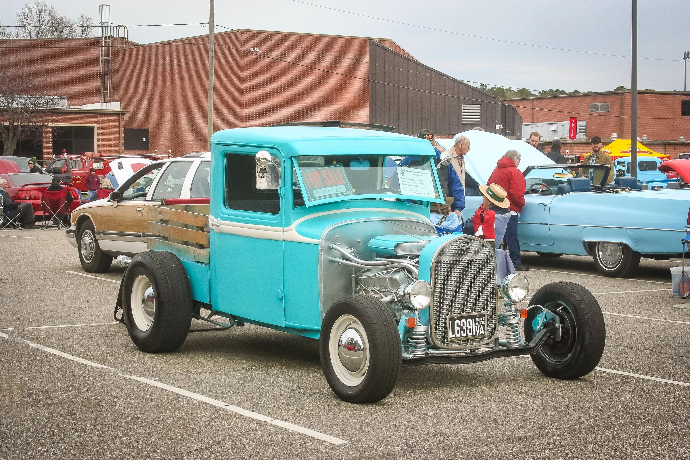 A vintage turquoise and cream pickup truck with an exposed engine, at a car show, surrounded by people and other classic cars.
