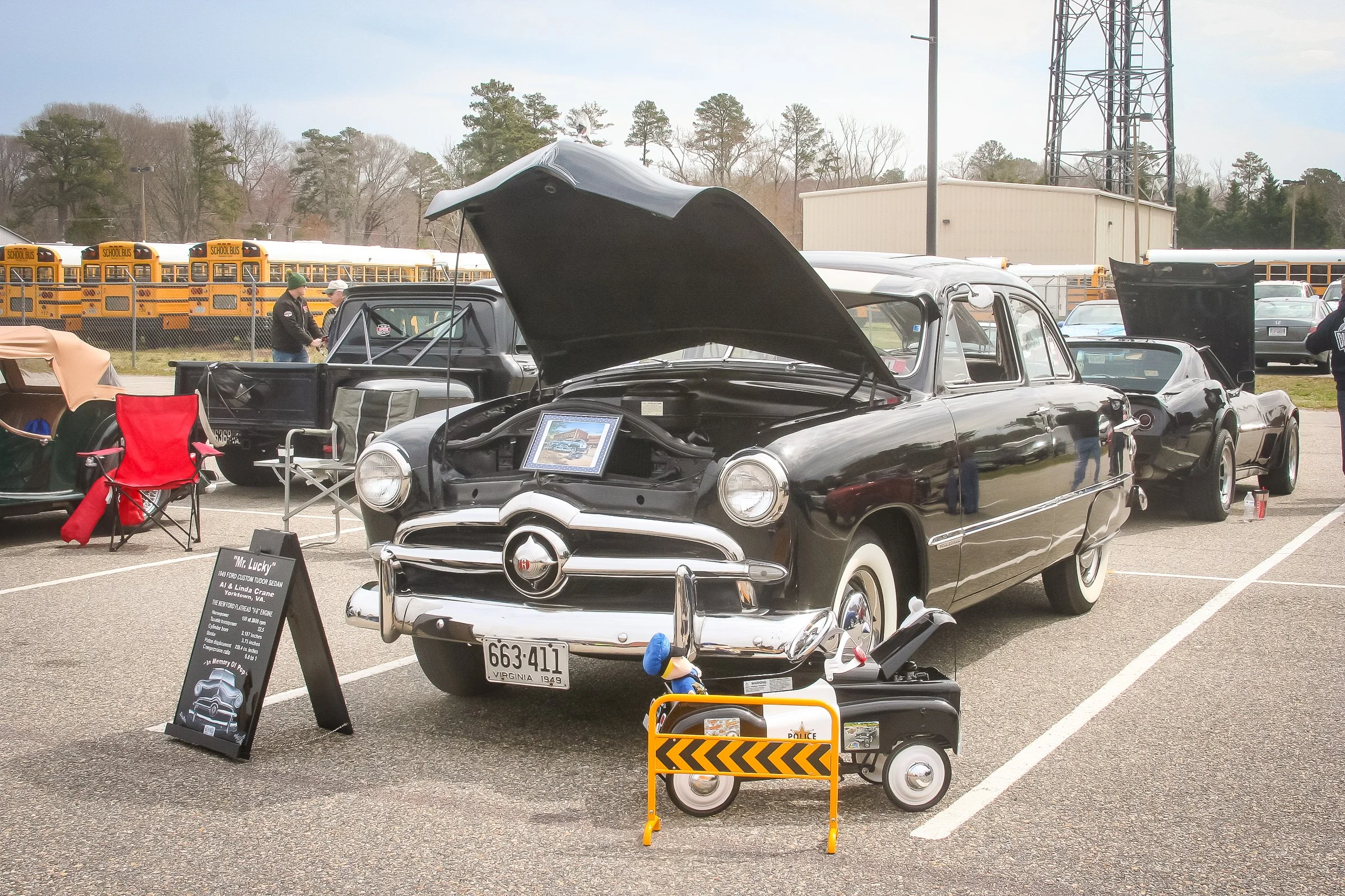 Display of a black vintage car with its hood open at a car show. The car has whitewall tires, chrome details, and a plaque with the name "Mr. Lucky"