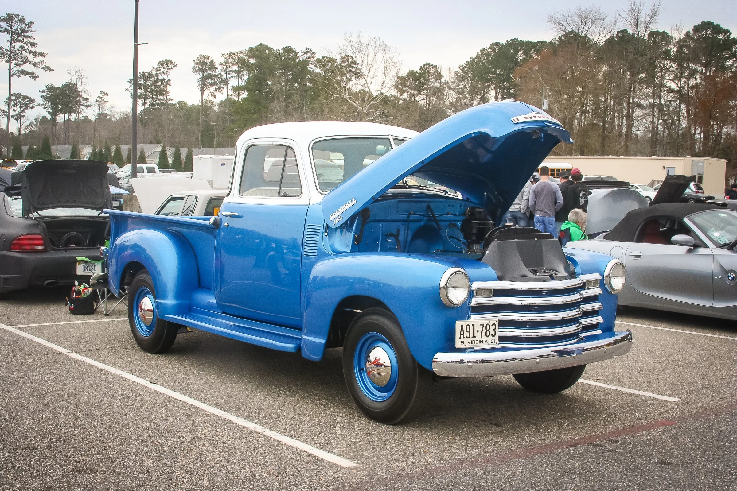 A vintage blue and white Chevrolet pickup truck with its hood open at an outdoor car show.