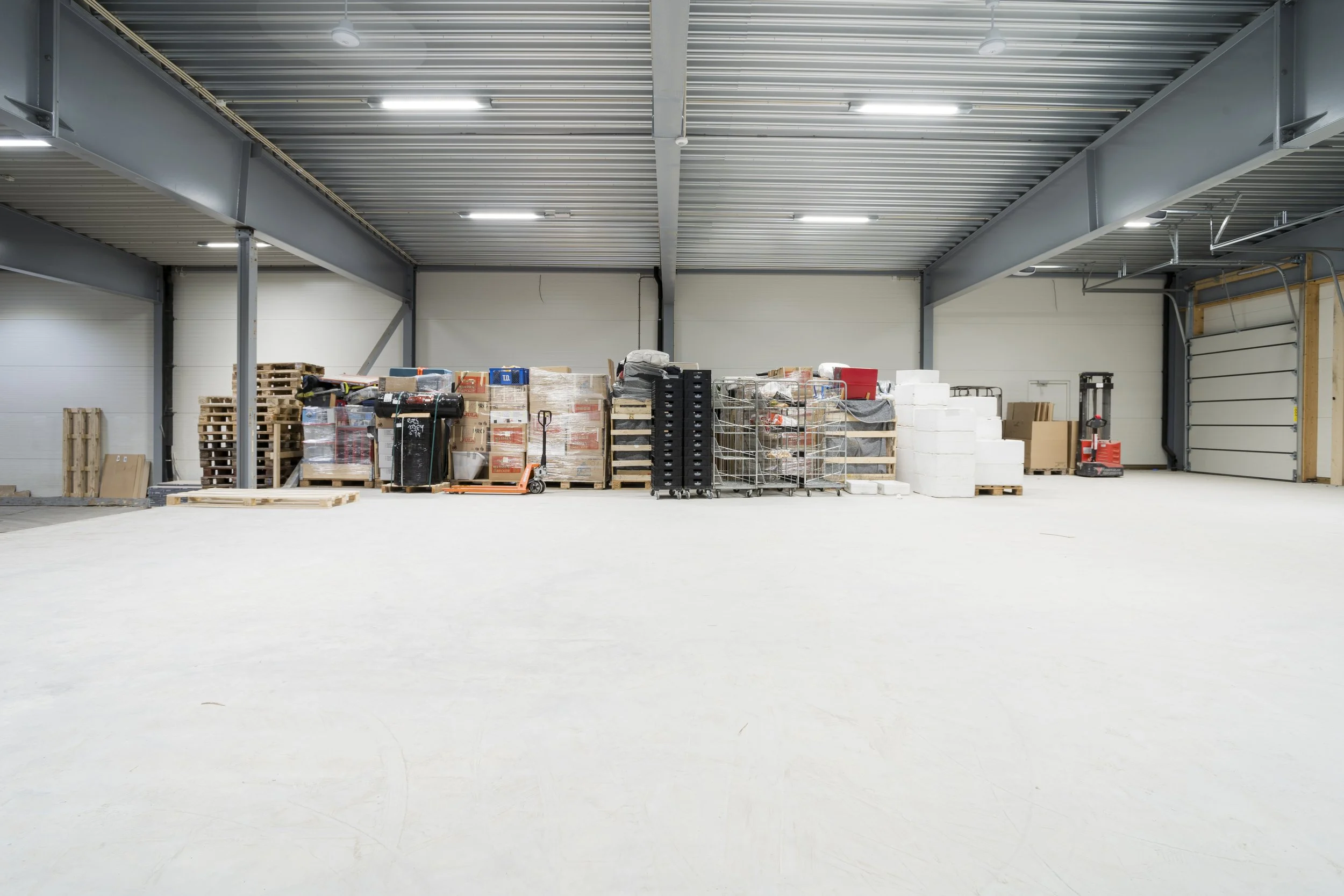 Innvendig i et tomt lager med ulike paller og lagringsutstyr mot veggen.