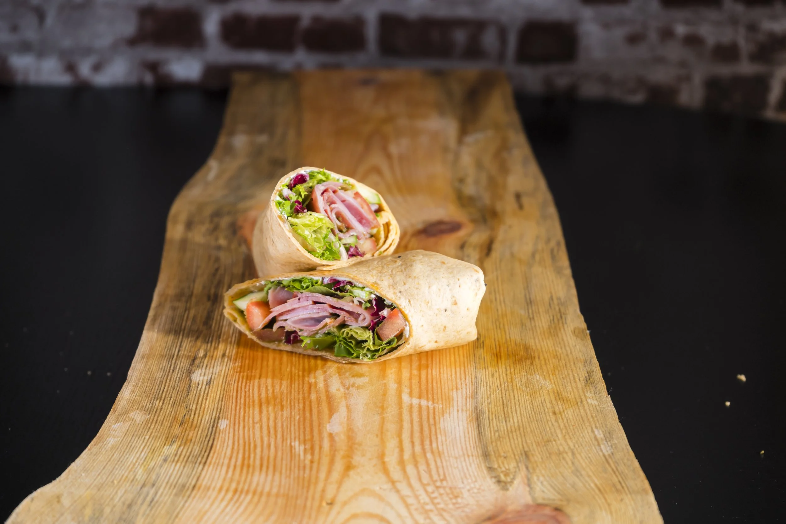 Wrap med assortert salat, kjøttpålegg og grønnsaker, plassert på en treplate. Matfoto for Snackyard Solsiden