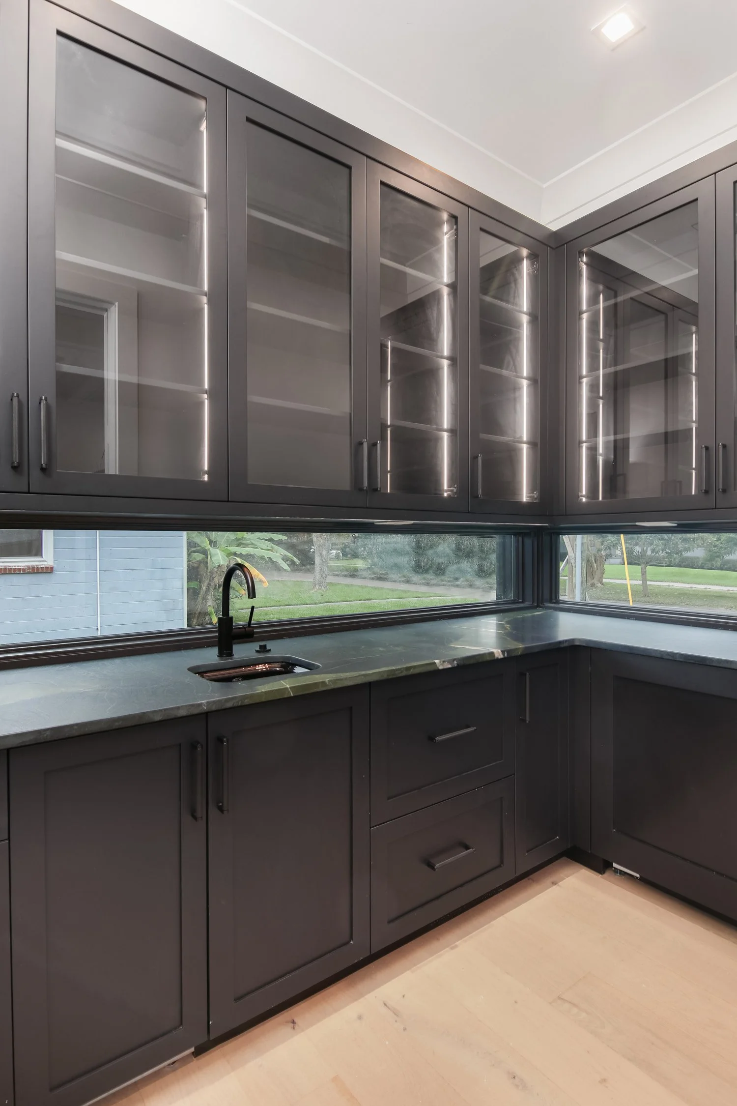Modern kitchen with black cabinets, marble countertop, black faucet, and windows overlooking a green yard.