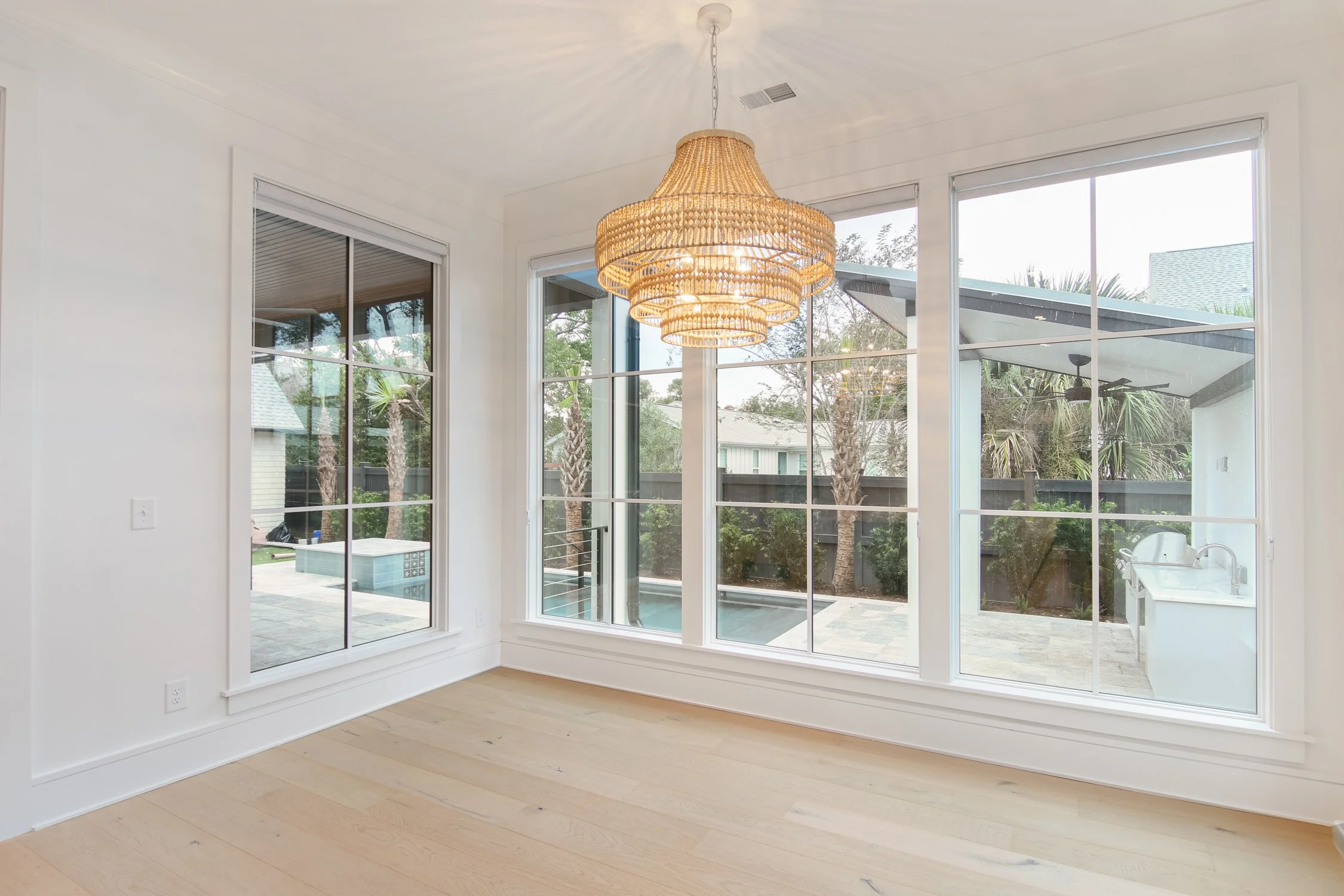 Empty room with large windows, wooden floor, and a woven pendant light
