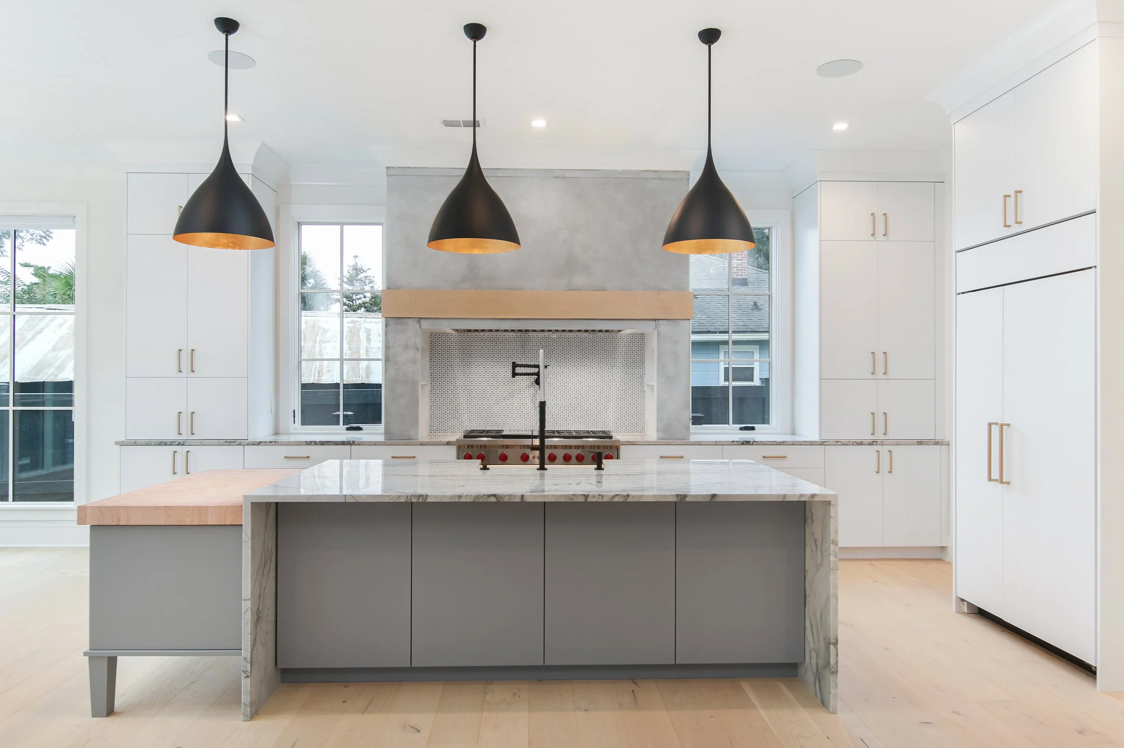 Modern kitchen with white cabinets, marble island, black pendant lights, and large windows.