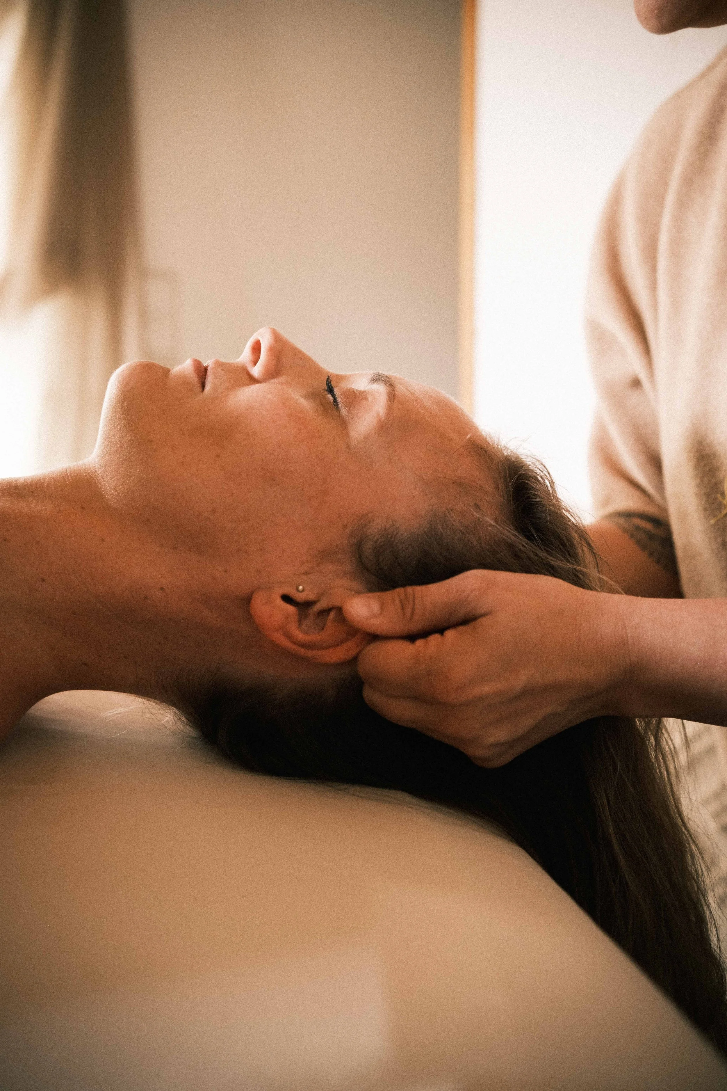 Nahaufnahme einer Person, die eine Massage am Kopf erhält, liegend auf einer Massagebank.