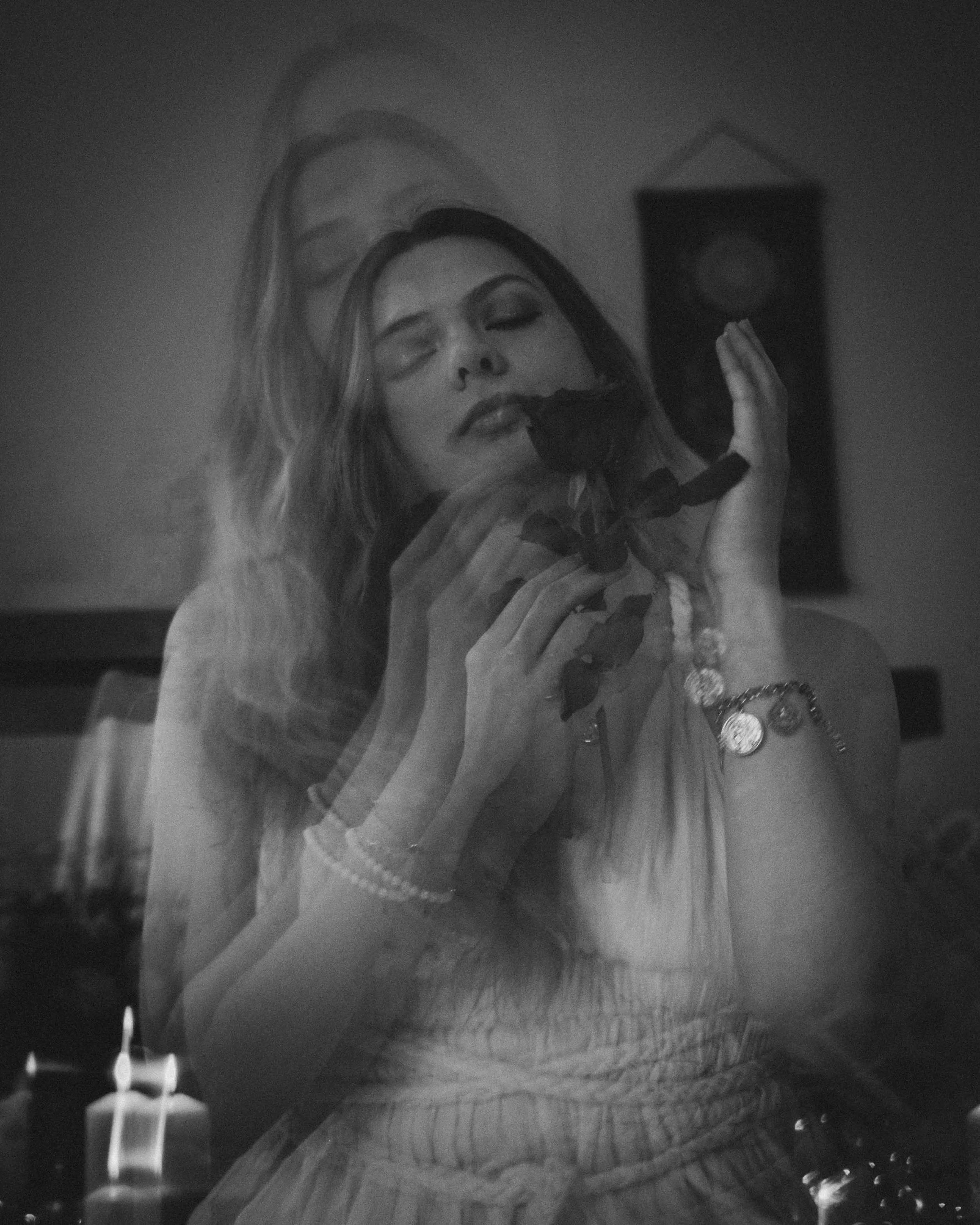 Ein schwarz-weiß Bild einer Frau, die eine Rose hält und ihre Augen geschlossen hat, mit mehreren Überlagerungen ihres Gesichts, was einen träumerischen Effekt erzeugt.