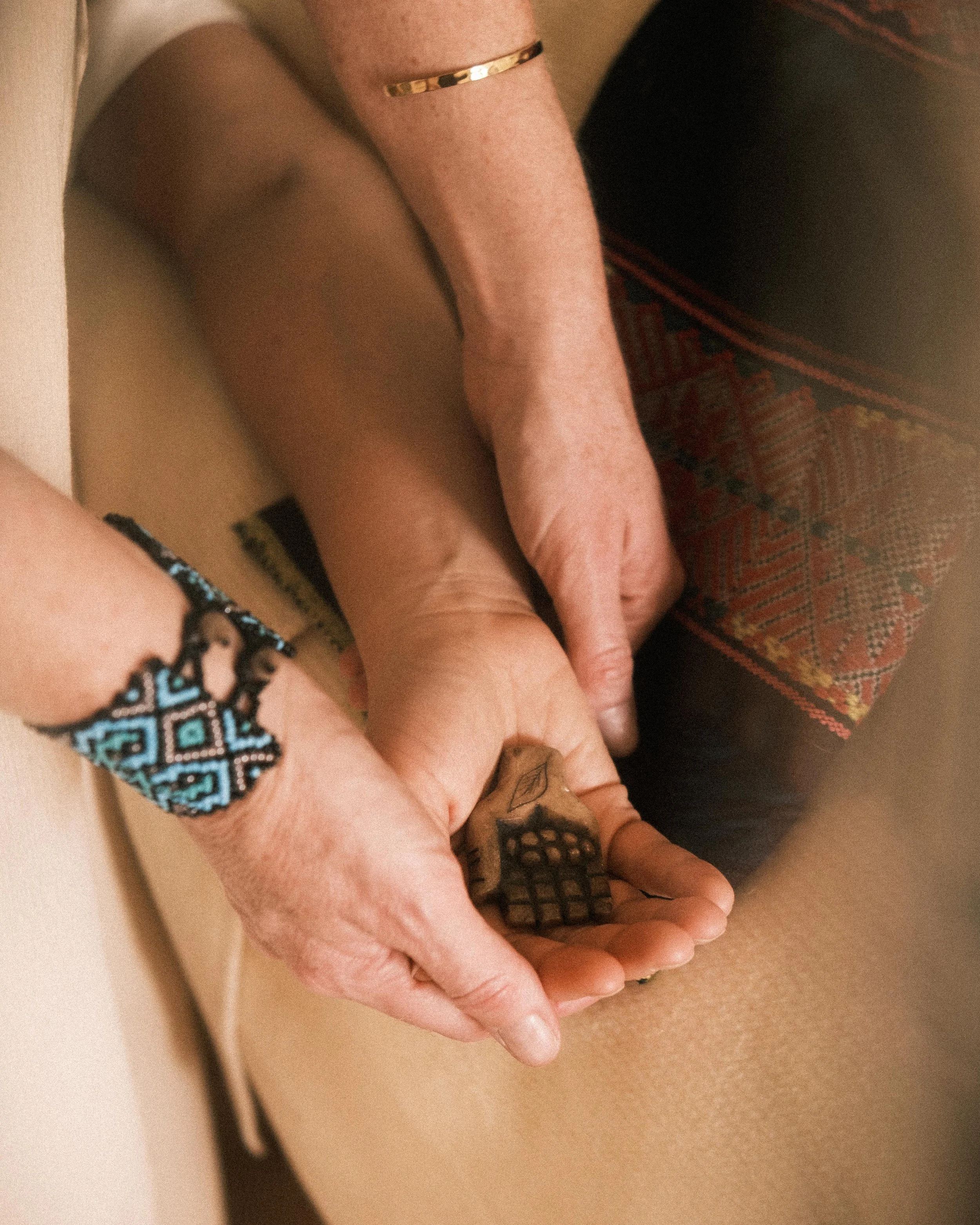 Nahaufnahme von zwei Händen, die ein geschnitztes Holzstück in Form einer Hand halten. Eine Person trägt ein Armband mit ethnischem Muster.