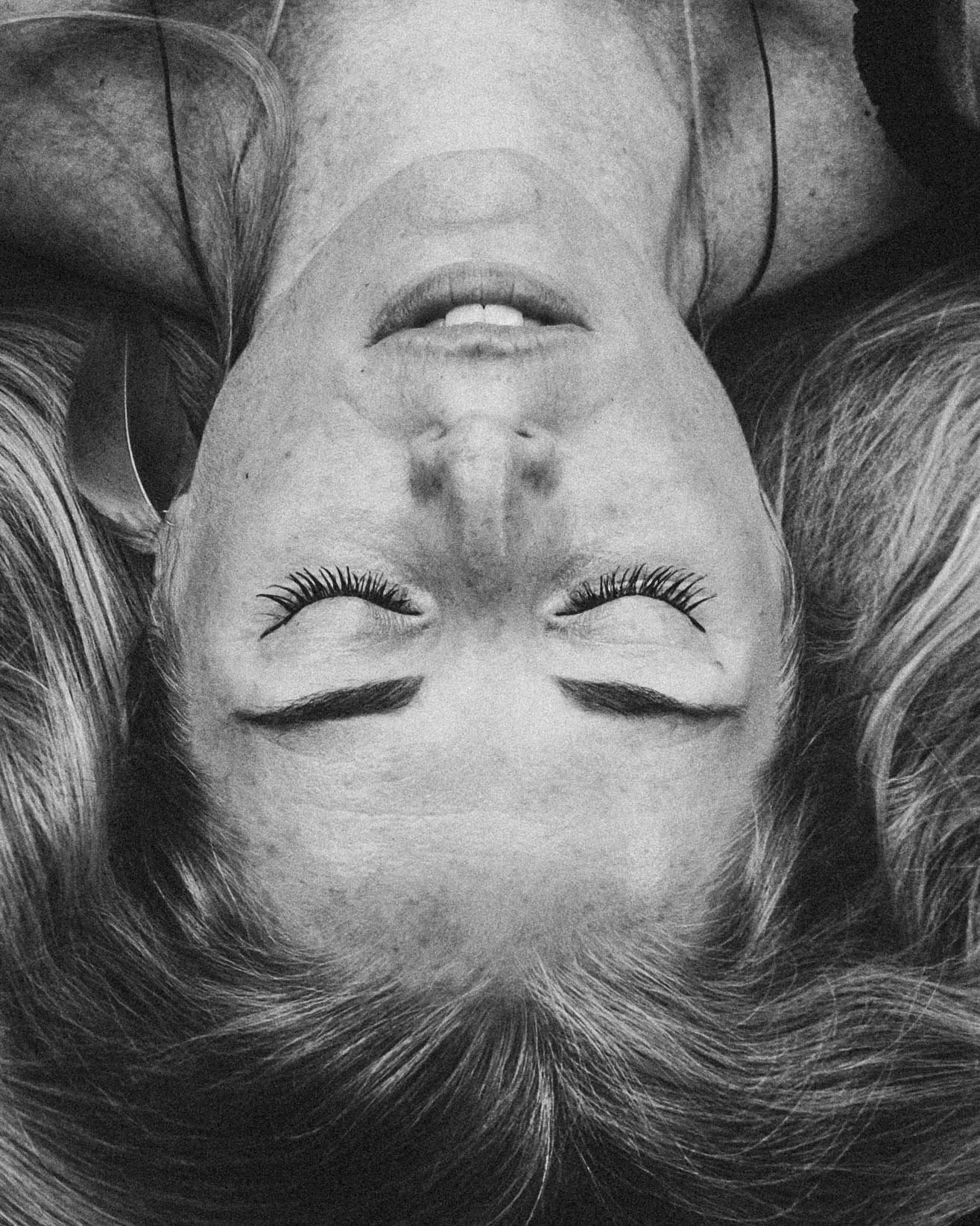 Schwarz-Weiß-Fotografie eines Frauenporträts, aufgenommen aus der Vogelperspektive, mit durchdringendem Blick und langen Wimpern.