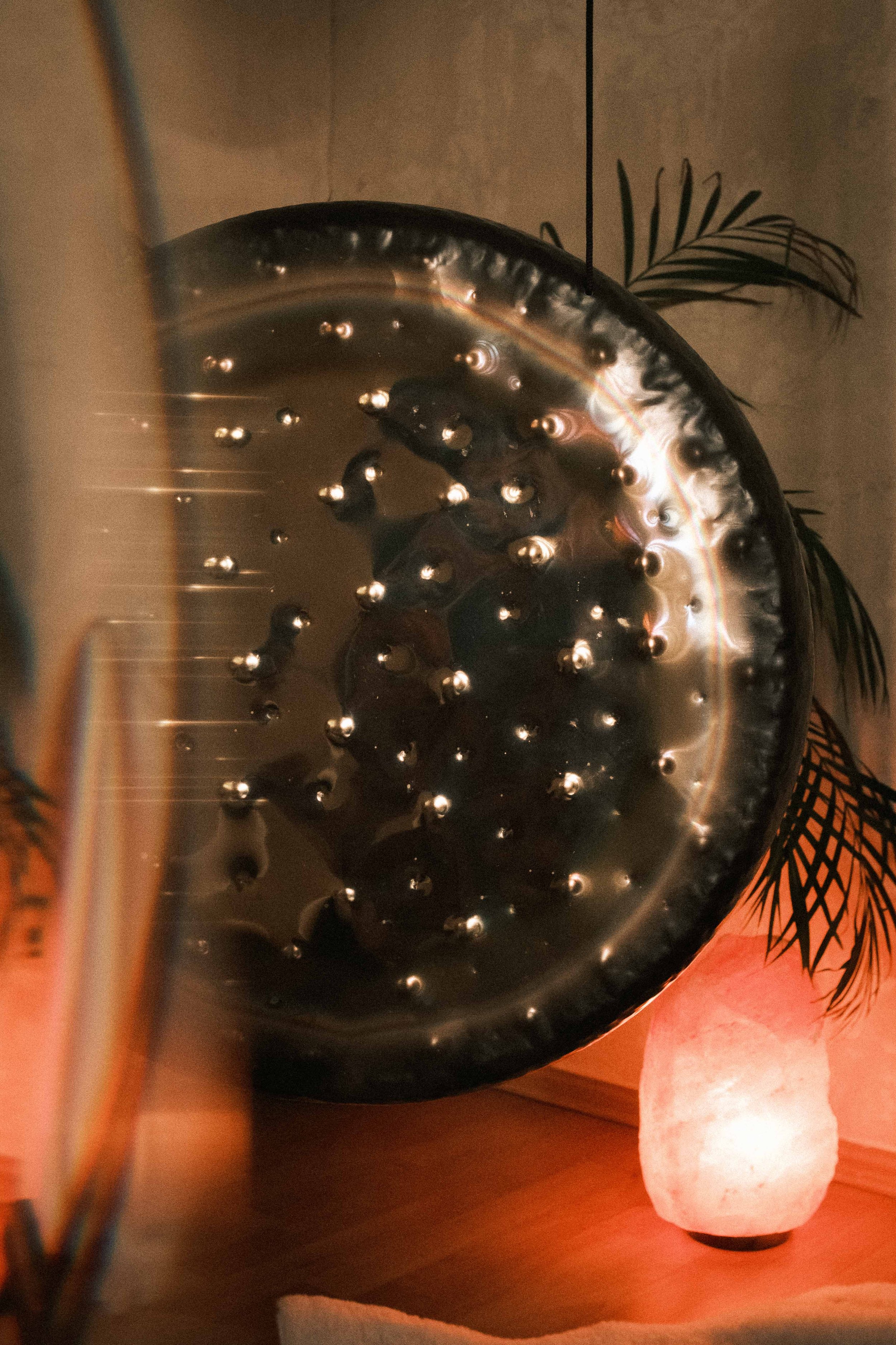 Eine große, runde, schwarze Metallwanne mit Wasser und mehreren schwarzen Steinchen. Im Hintergrund eine Stehlampe in Form eines weißen Steins und einige grüne Pflanzen. Die Szenerie wirkt ruhig und dekorativ.