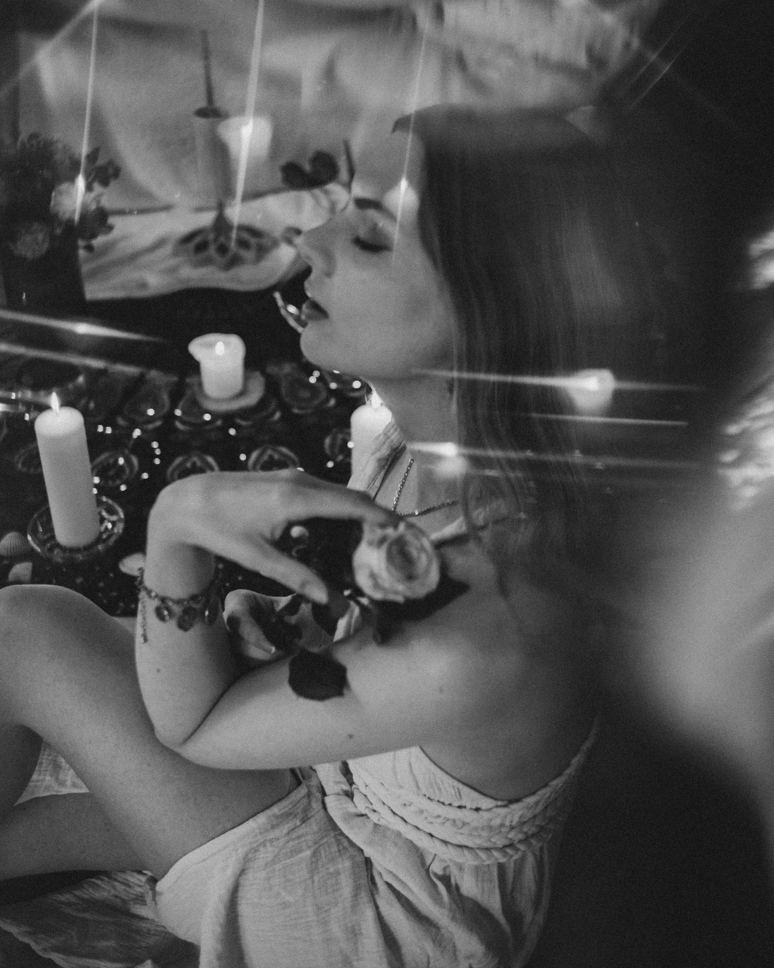 Schwarz-weiß-Foto einer Frau mit langen Haaren, die eine Rose hält, umgeben von Kerzen und Dekorationen.