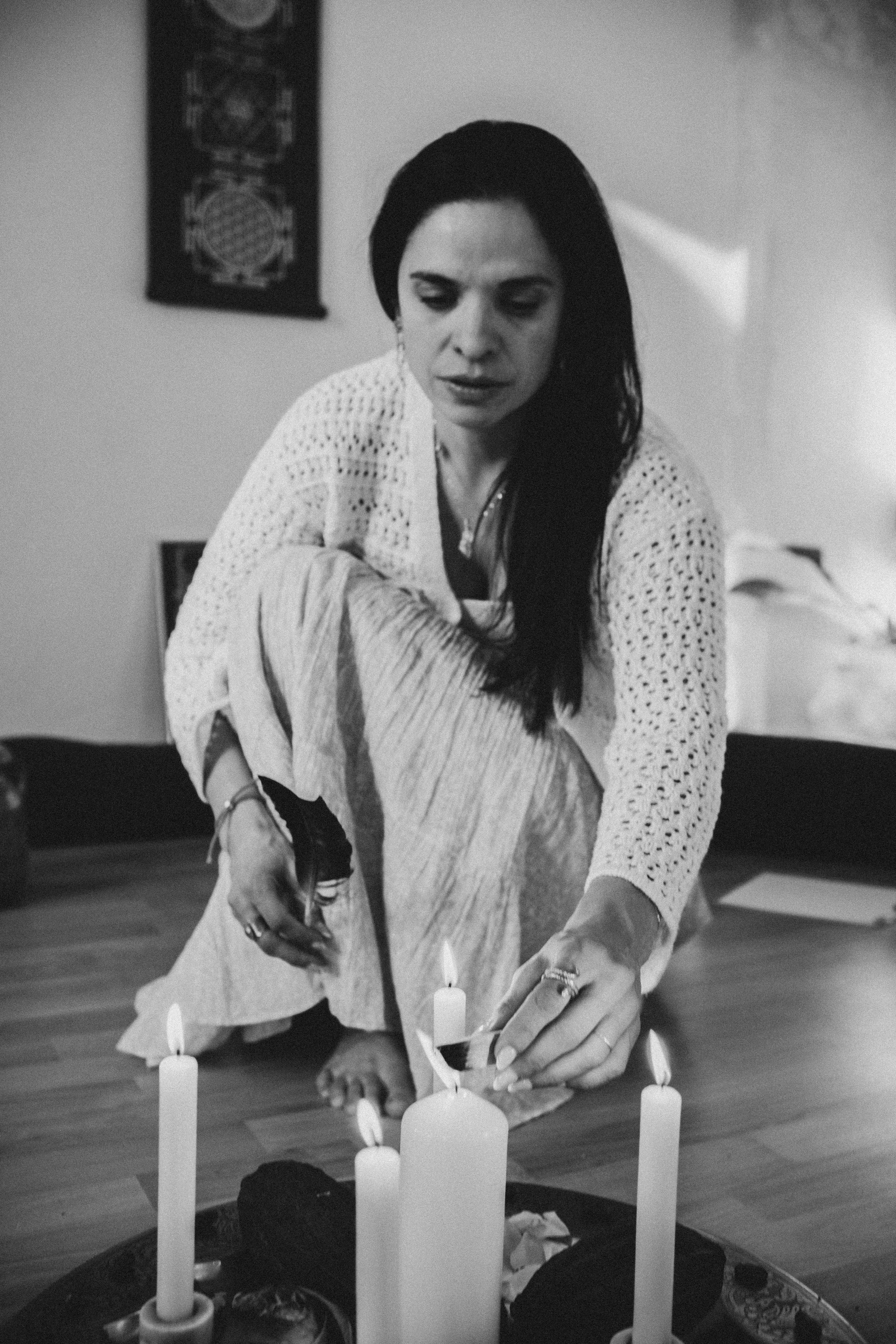 Schwarz-weiß-Foto einer Frau, die in der Kreismitte eines zeremoniellen Raums Kerzen anzündet.