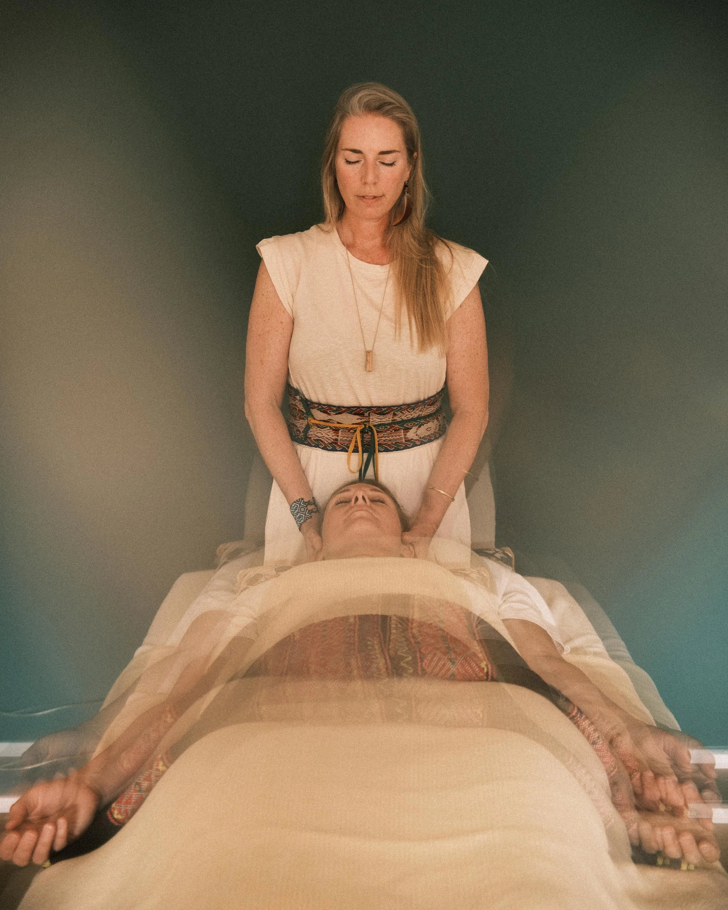 Eine Schamanin hält den Kopf ihrer meditativ vor ihr liegenden Klientin in einer Healing Session.