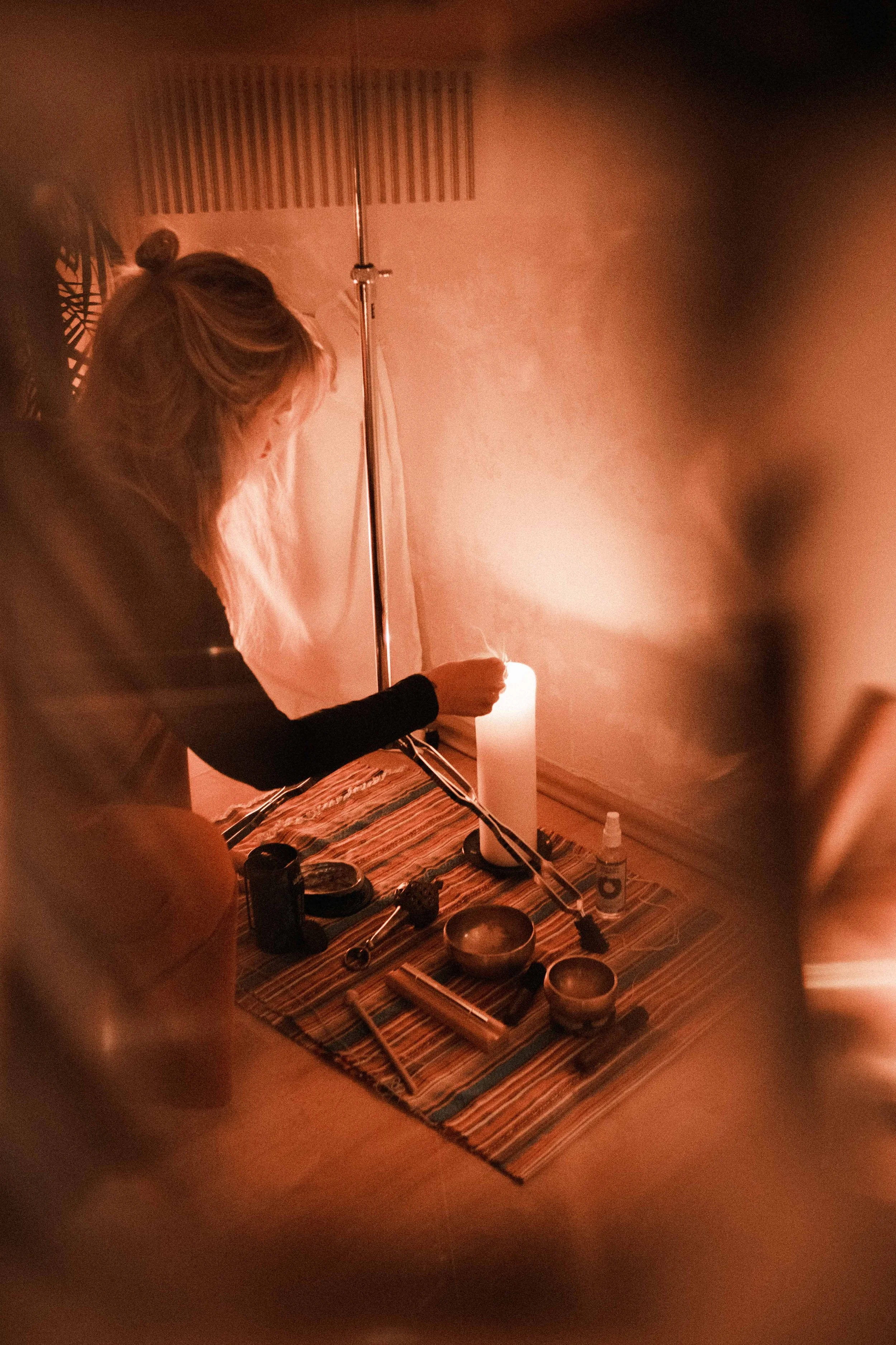 Frau sitzt bei Kerzenlicht umgeben von spirituellen Gegenständen auf einem Tisch.