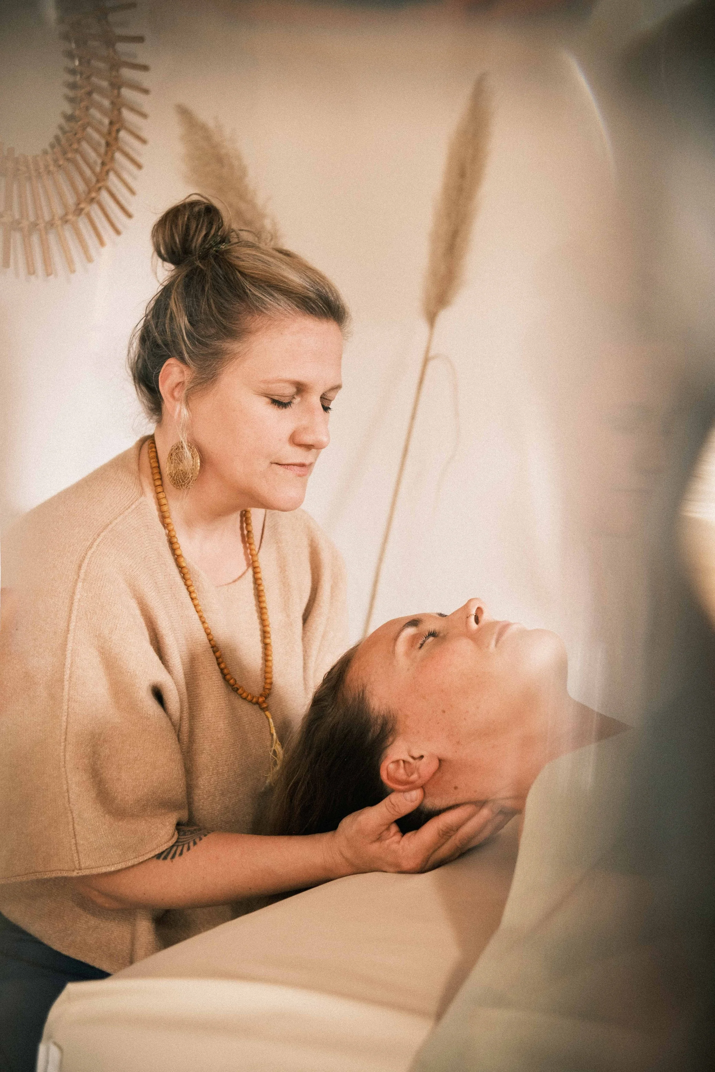 Frau liegt entspannt auf einer Massagebank, während eine Therapeutin sie im Nackenbereich massiert.