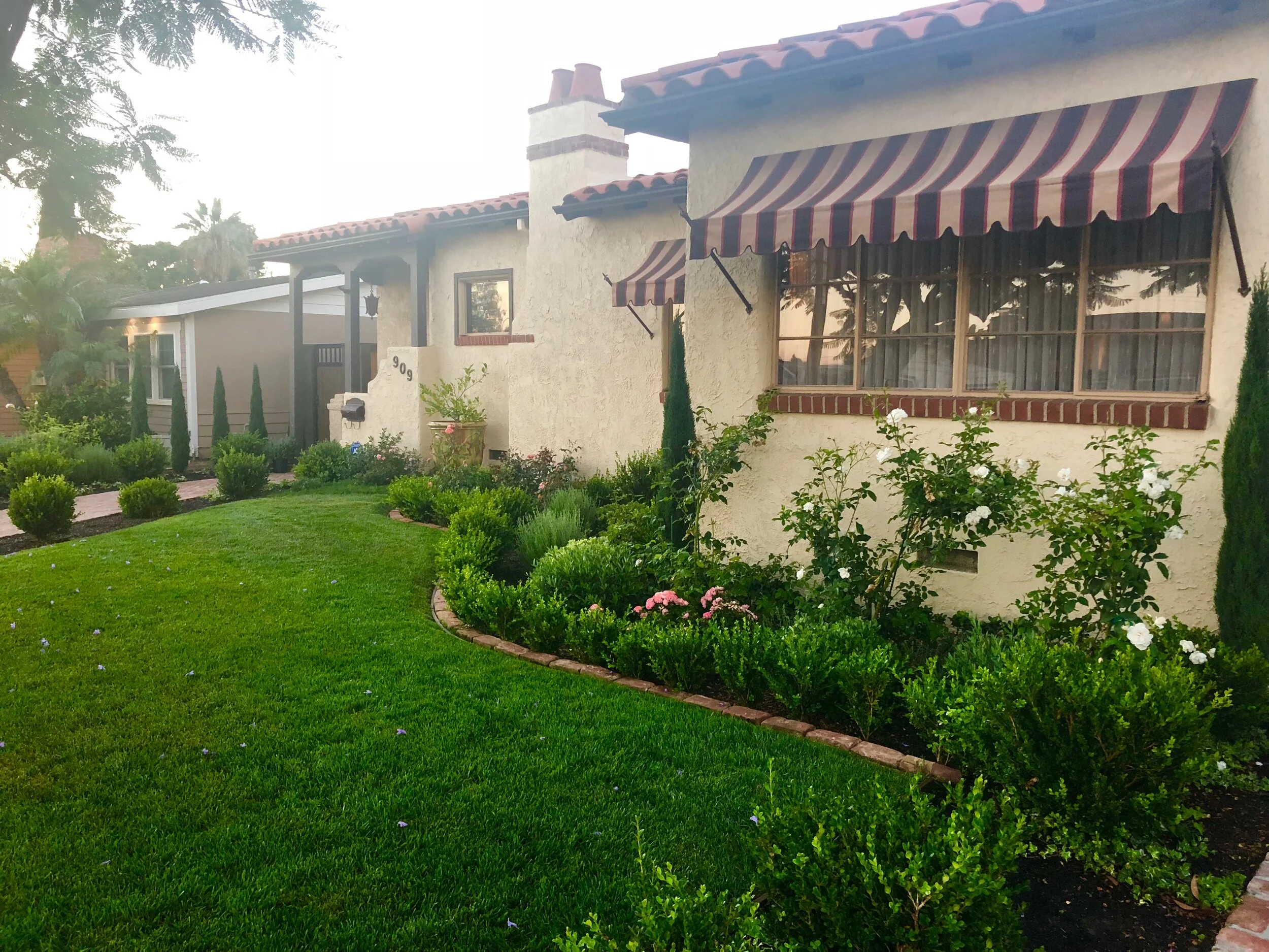 Boxwood hedges, roses, cypress, and topiaries complement the romantic Mediterranean palette of this vintage 1930s Spanish home