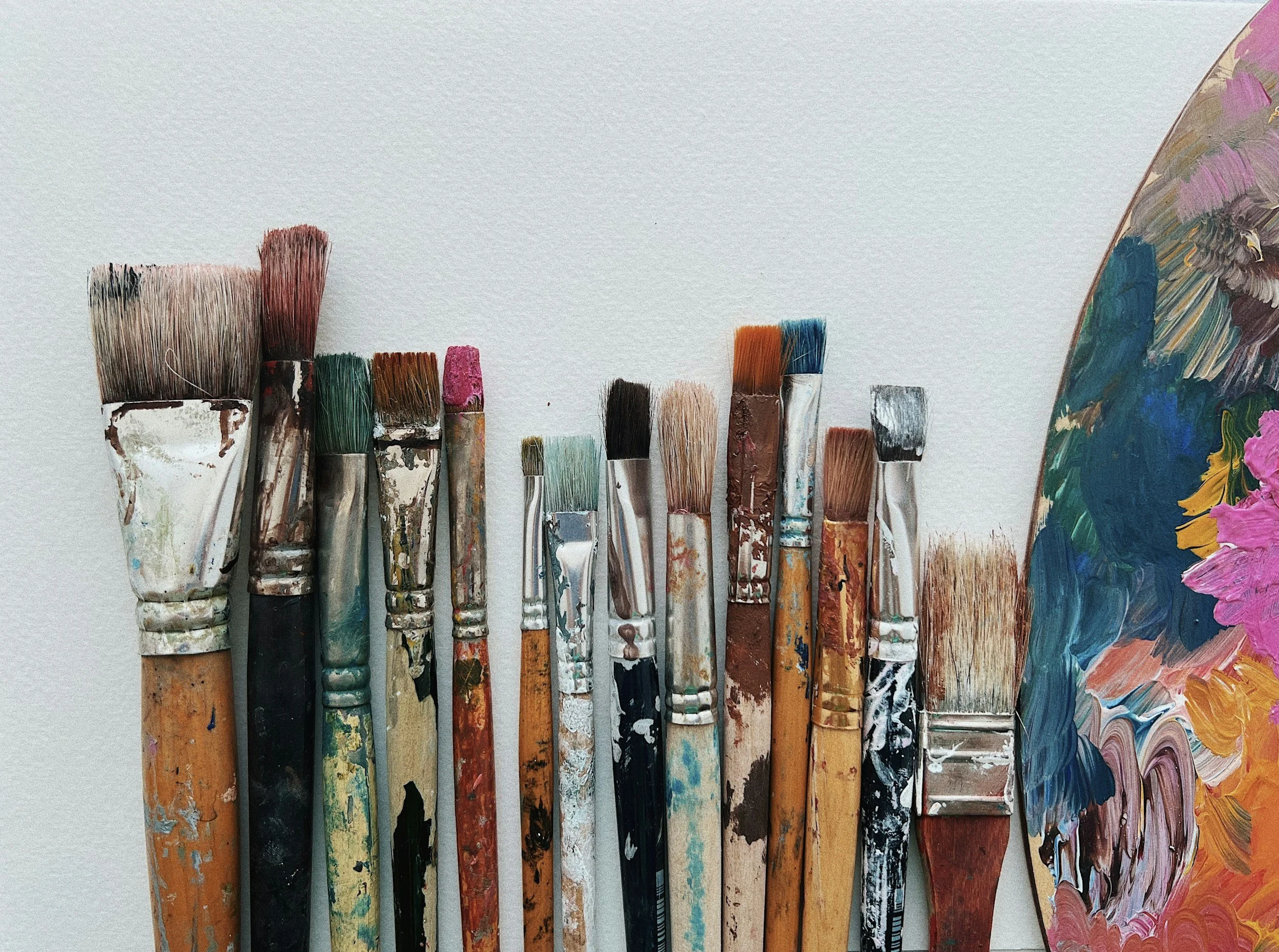 Collection of used paintbrushes with various bristle sizes and colors, and a palette with colorful paint strokes on the right side.
