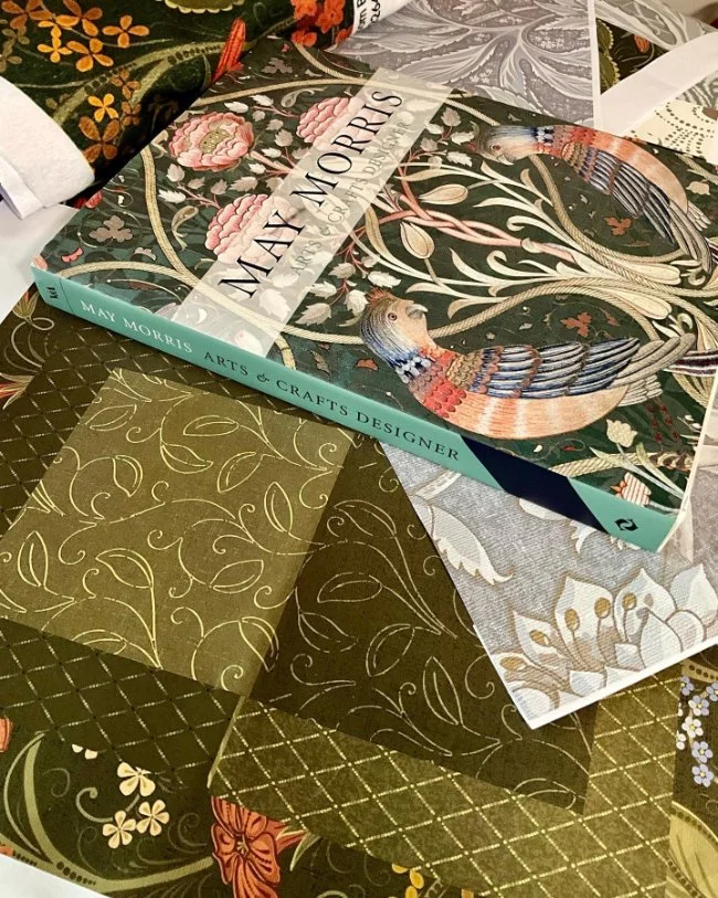 Arts and Crafts design reference book alongside fabric pattern swatches used for developing heritage-inspired collections.