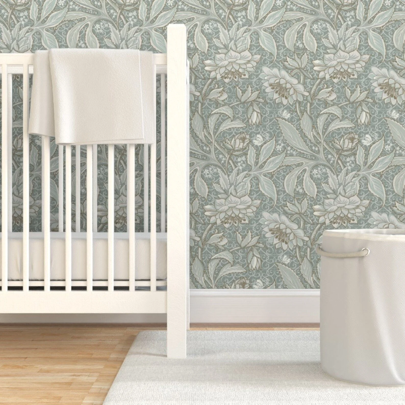 A white crib with a white blanket draped over one side, set against a floral wallpaper with shades of blue, white, and gray. Designed by Wild Geranium Design.