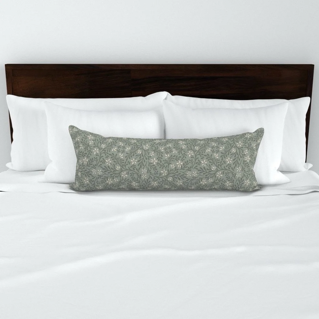 A bed with white sheets, white pillows, and a decorative green pillow with a floral pattern, against a plain white wall. Designed by Wild Geranium Design.