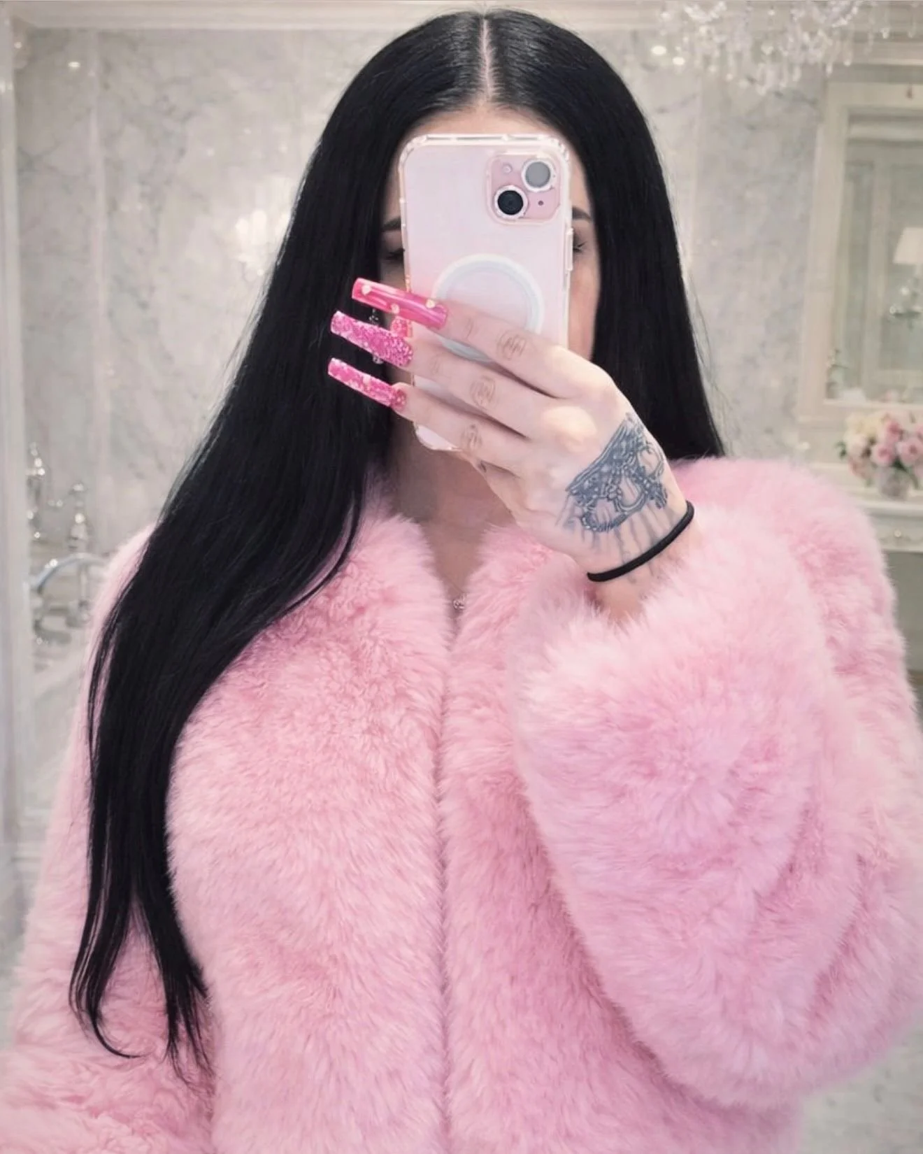 Mirror selfie in a pink fur coat, with long black hair and pink, glittery nails.