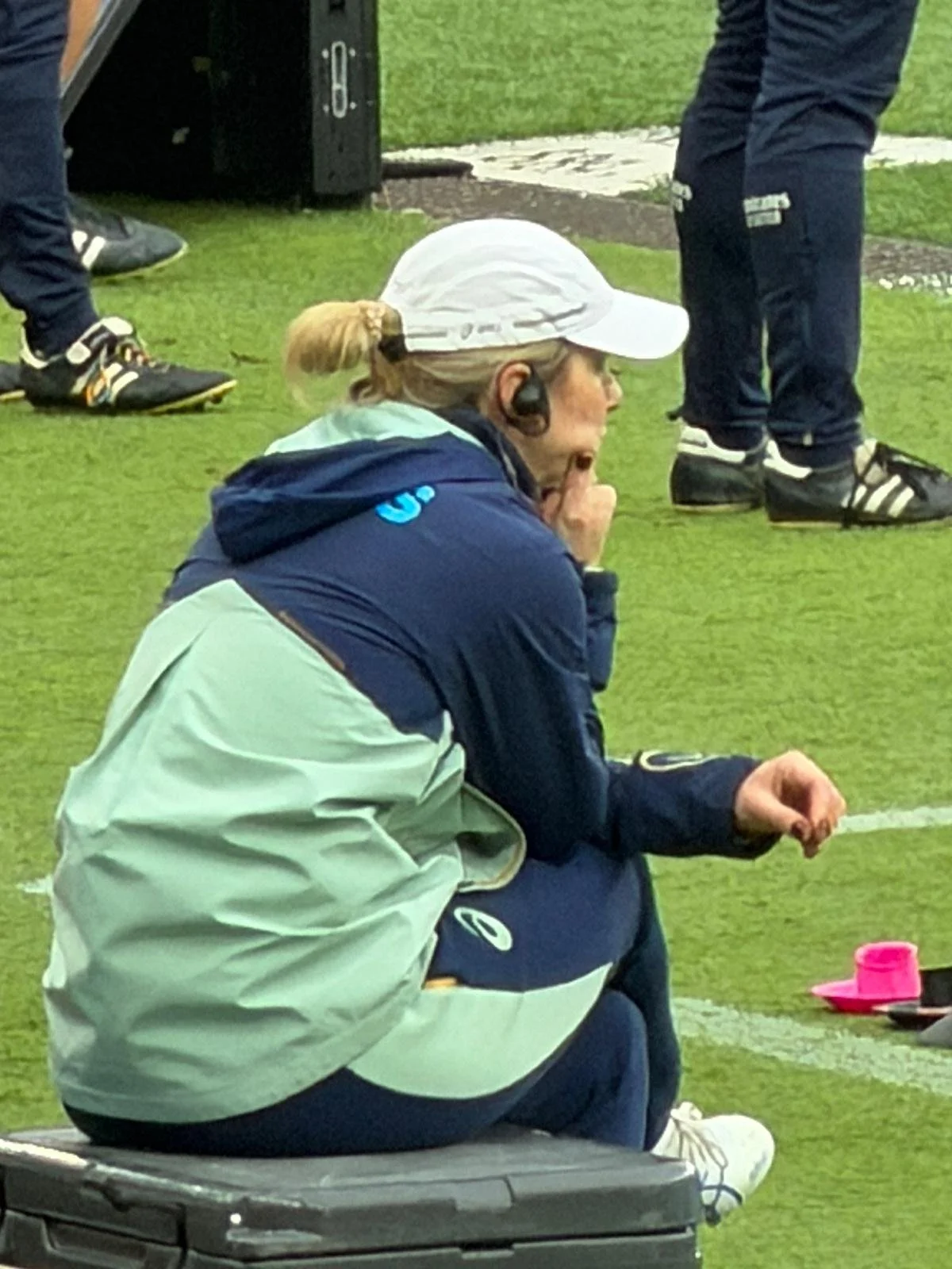 Eliza Freney sits sideline for Wallabies game against the French National Team, dressed in Asics wearing  a headset and providing sports nutrition services.