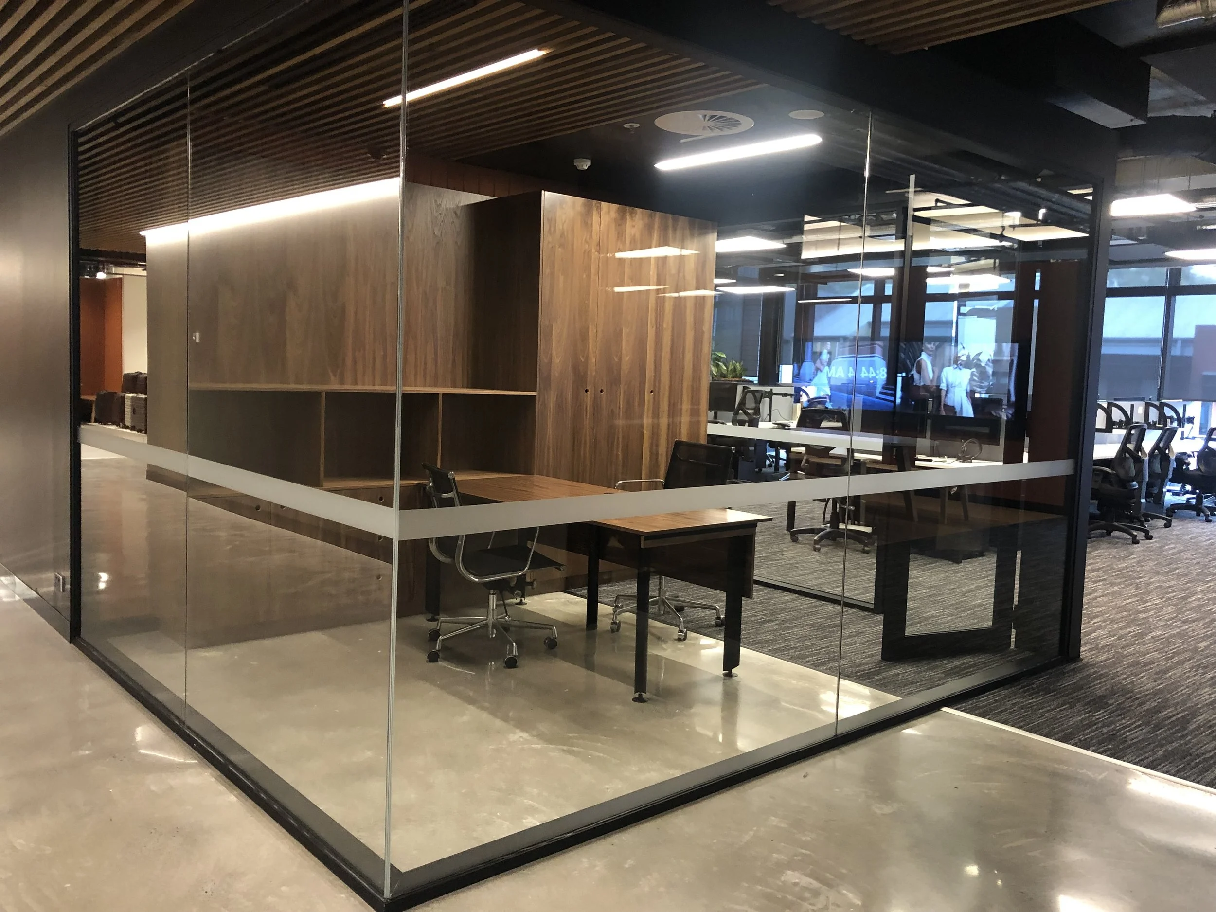 Empty office conference room with glass walls, wooden accents, a small table, and office chairs inside.