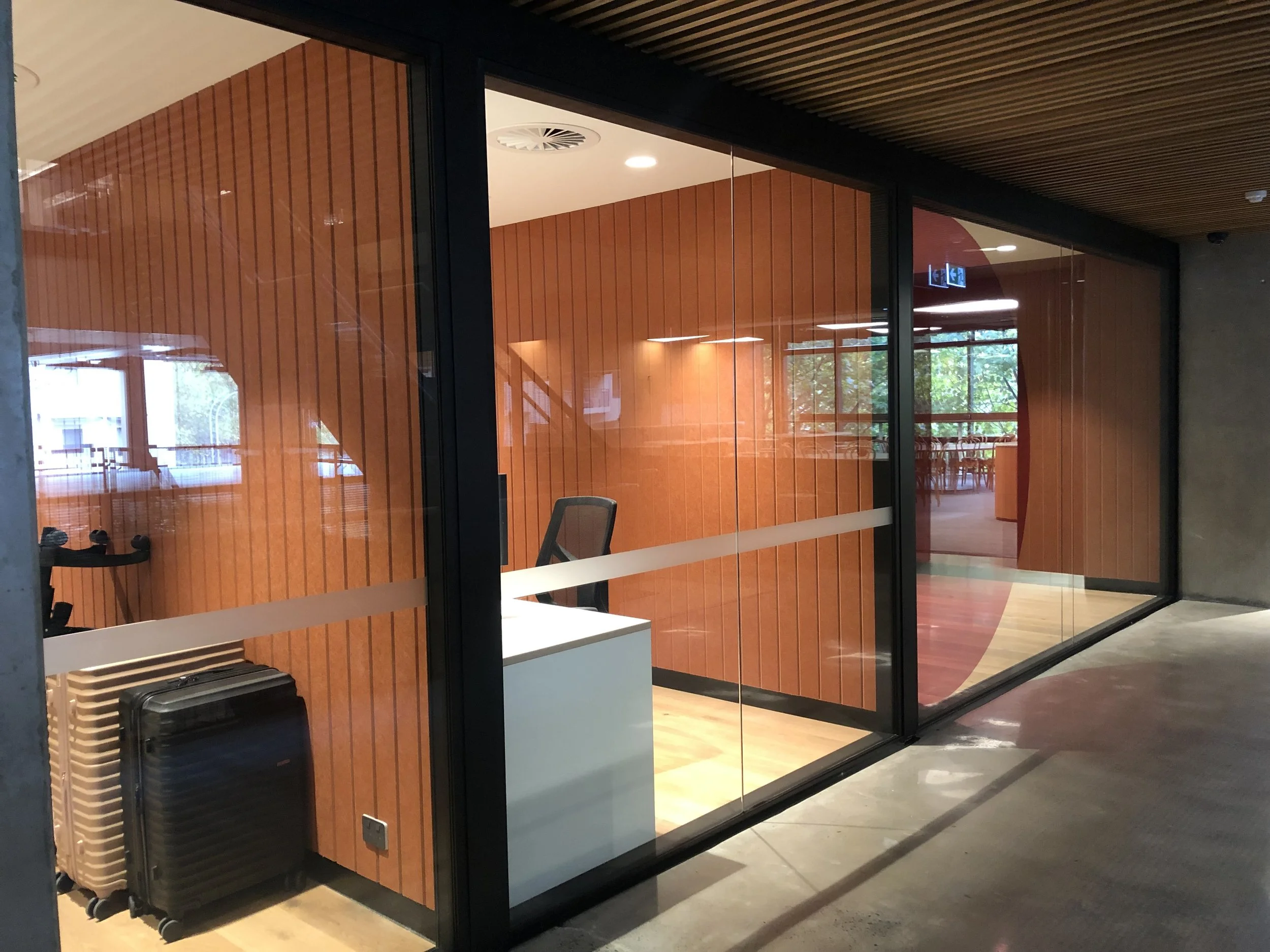 Empty office reception area with a desk, an office chair, and two suitcases in front of a glass wall with wooden paneling inside.