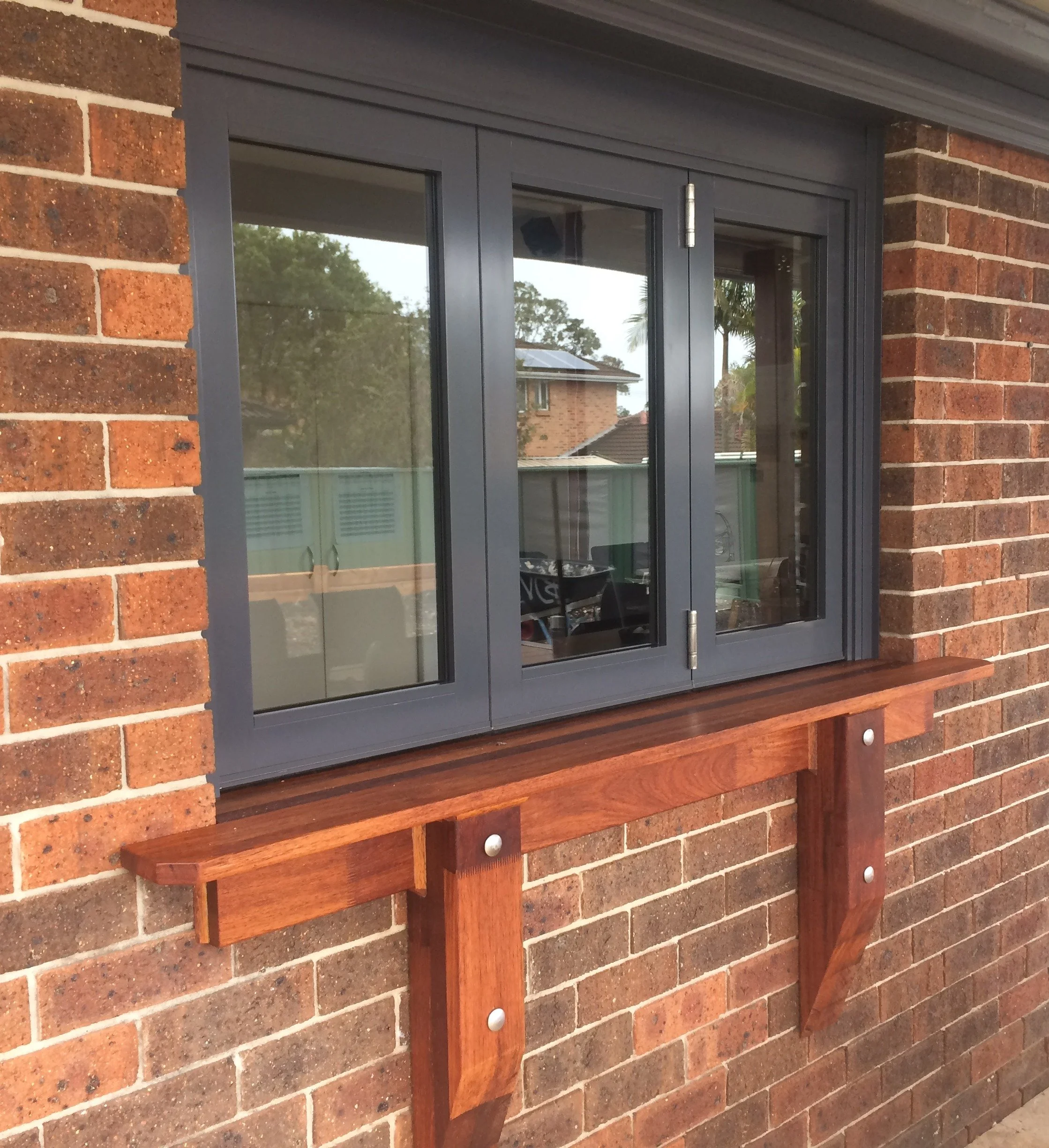 A brick house wall with a grey window and a wooden window sill and support brackets.