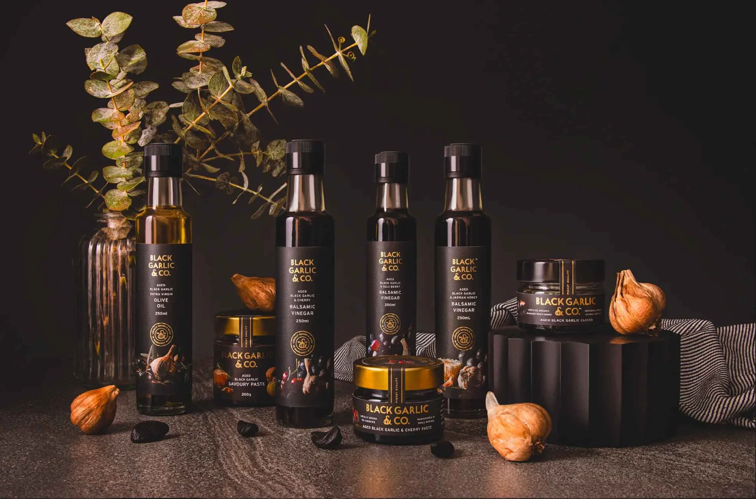 A stylised photograph showcasing Black Garlic & Co's range of pastes, olive oils and balsamic vingear