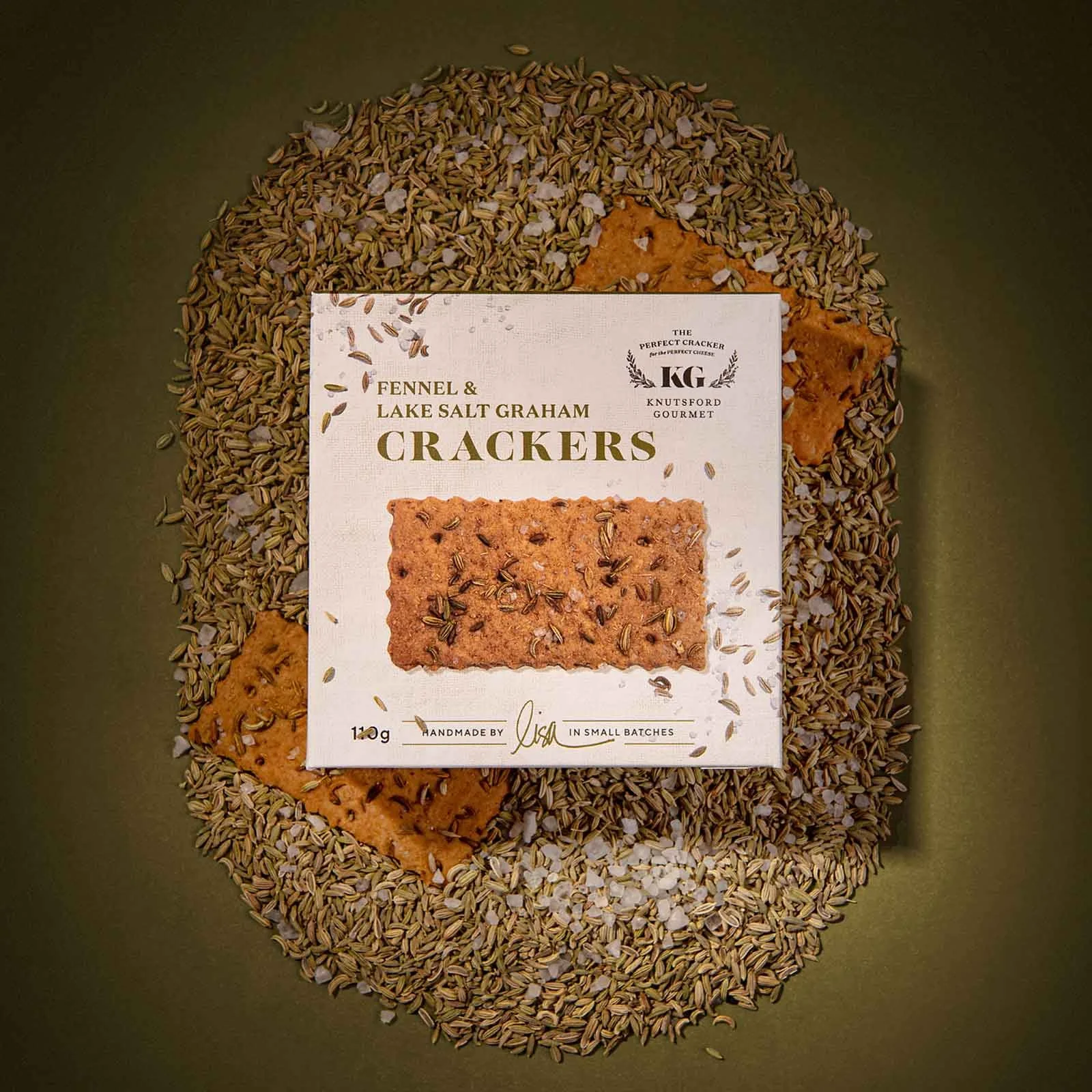 A stylished photograph of Knutsford Gourmet's Fennel and Lake Salt Graham Crackers packaging, positioned on top of the crackers and fennel seeds and salt flakes