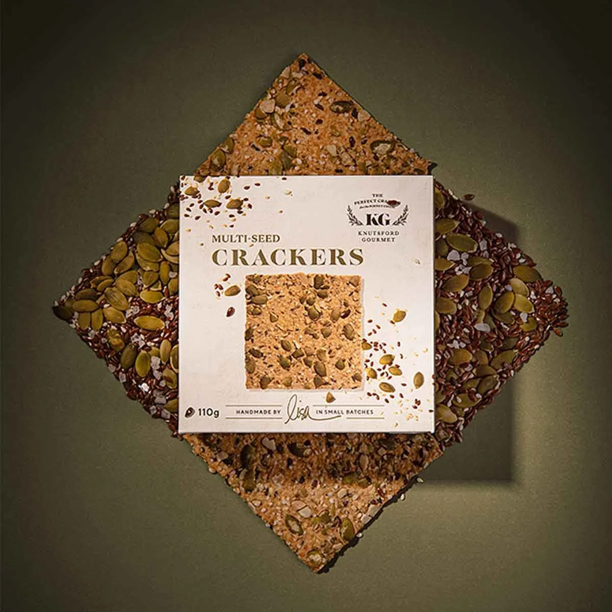 A stylished photograph of Knutsford Gourmet's Multi Seed Crackers packaging, positioned on top of the crackers and multi seeds that are the main ingredient in the crackers